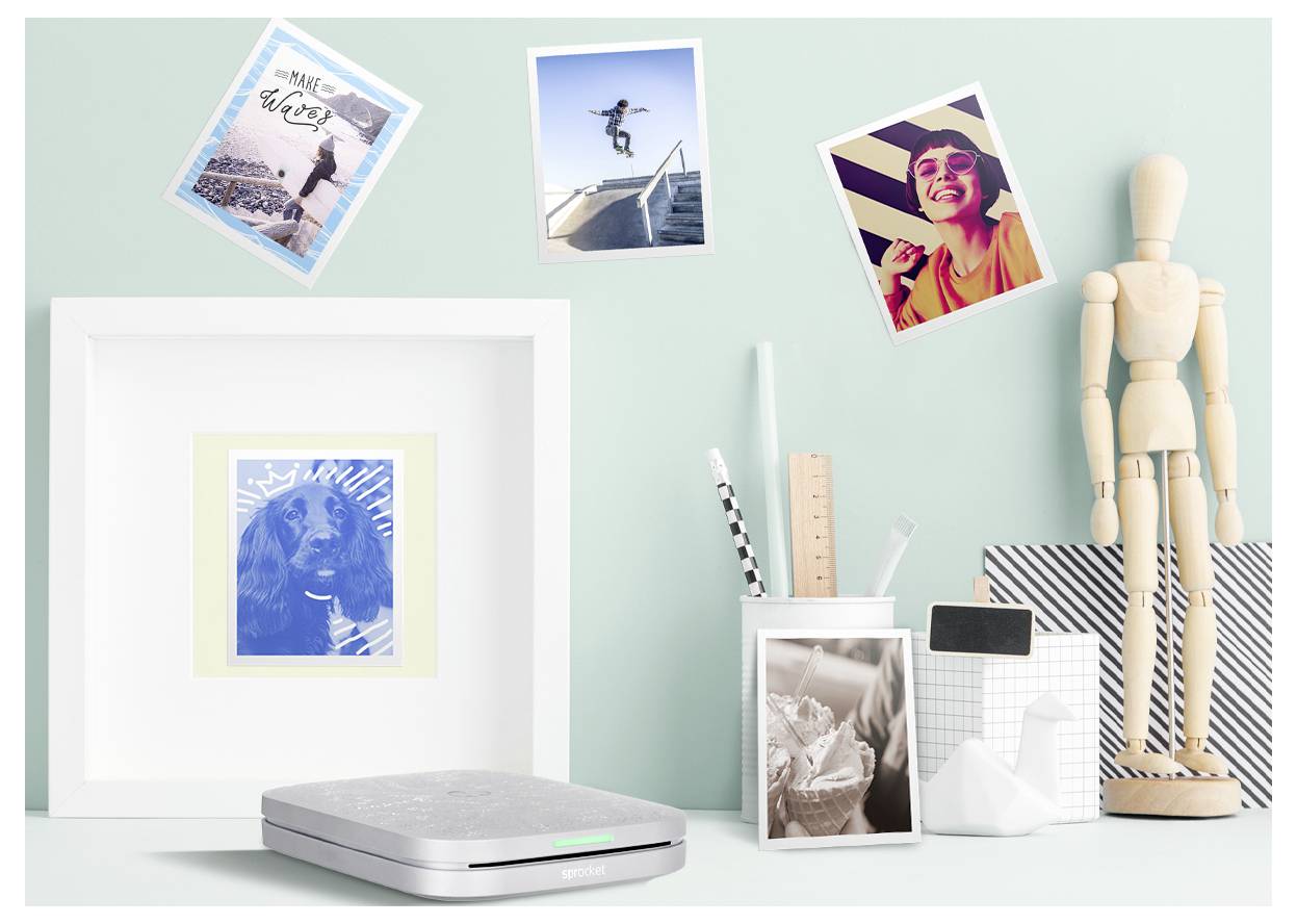 Arrangement de bureau stylisé avec art encadré, petites photos, un scanner, un pot à crayons, une boîte de mouchoirs et un mannequin articulé en bois contre un mur vert menthe.