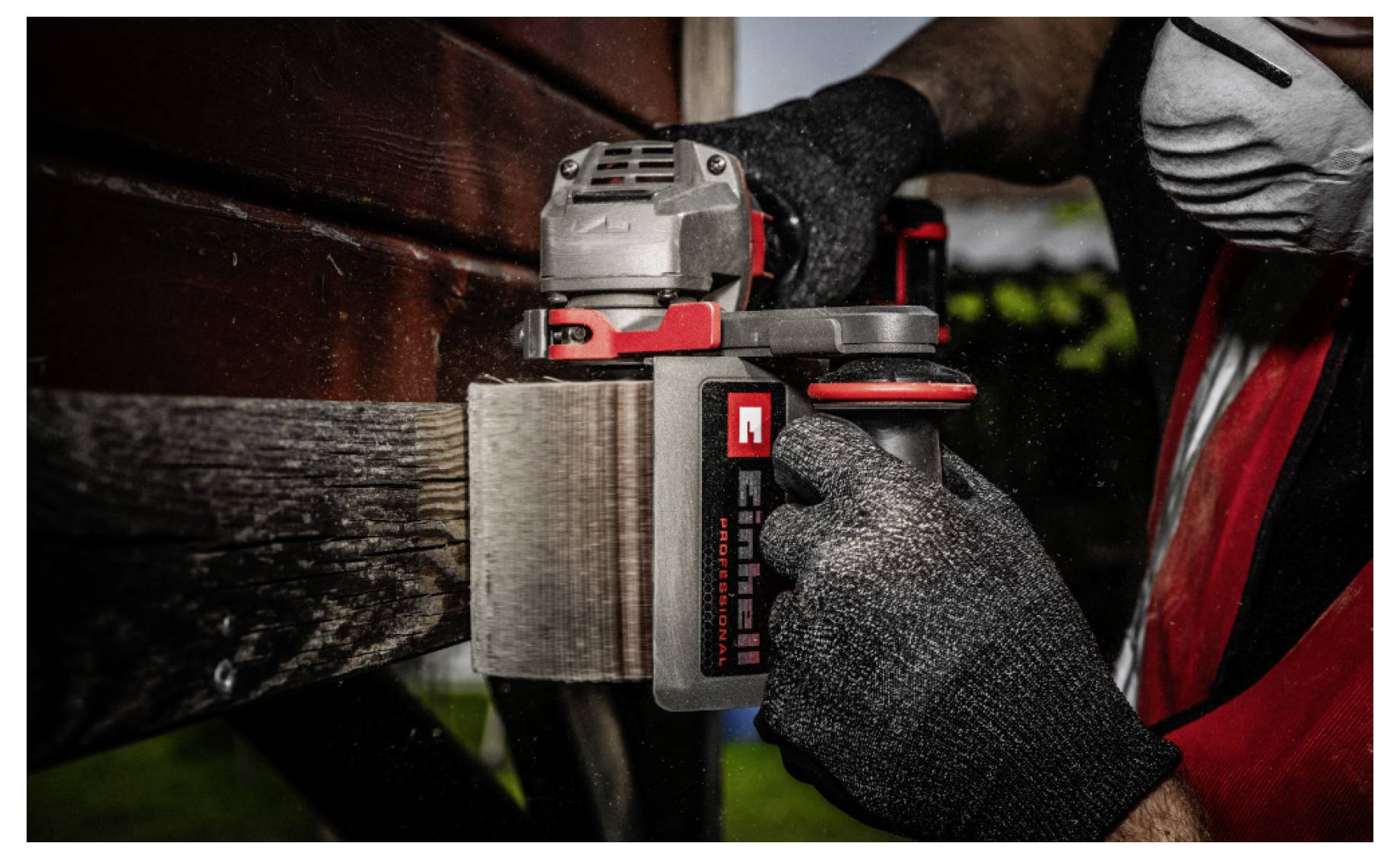Un ouvrier ponçant une surface en bois avec une ponceuse électrique portative, portant des gants noirs et un respirateur.