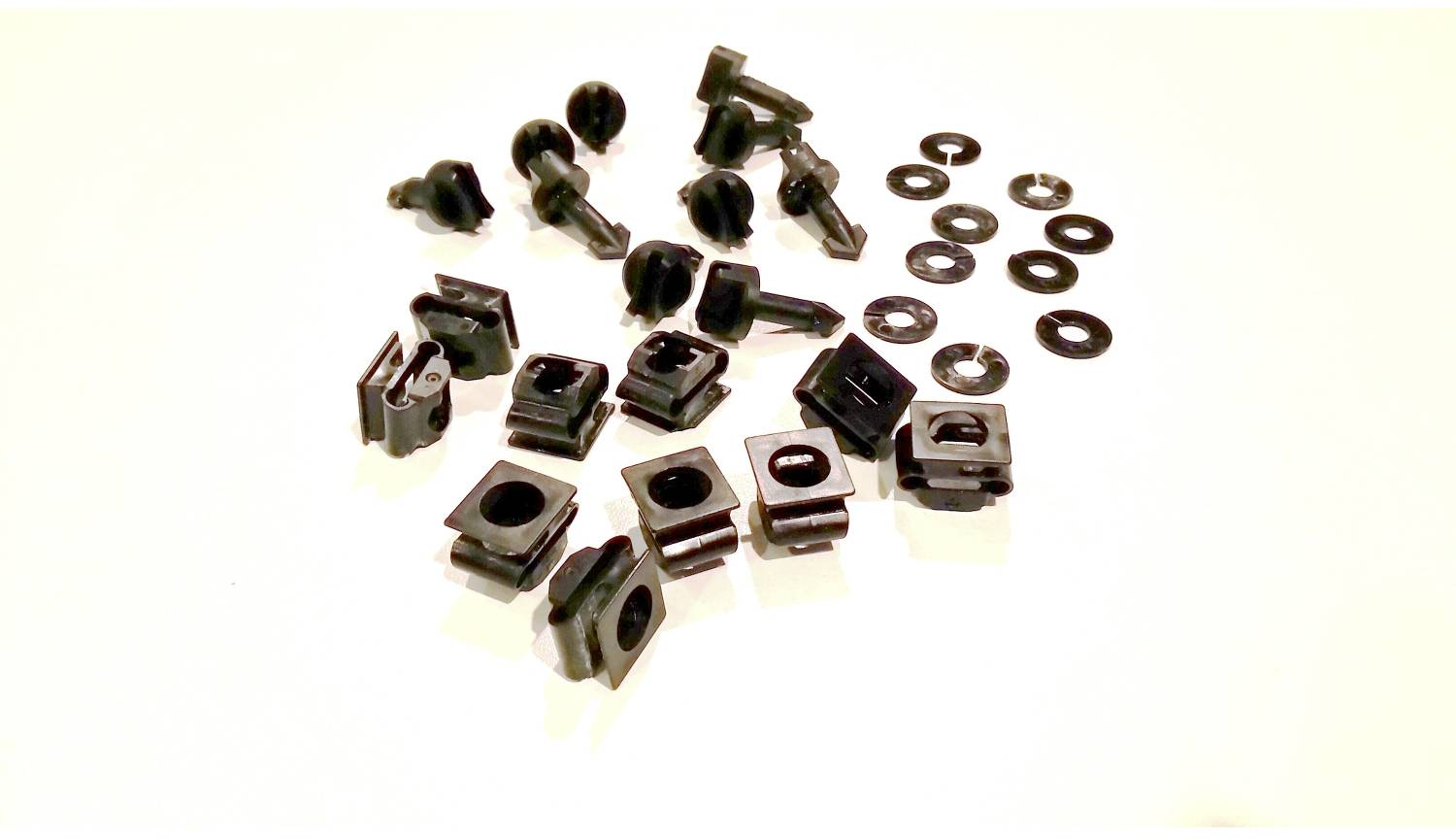 Verschiedene schwarze Kunststofffastener, Clips und Unterlegscheiben verstreut auf einer weißen Oberfläche.
