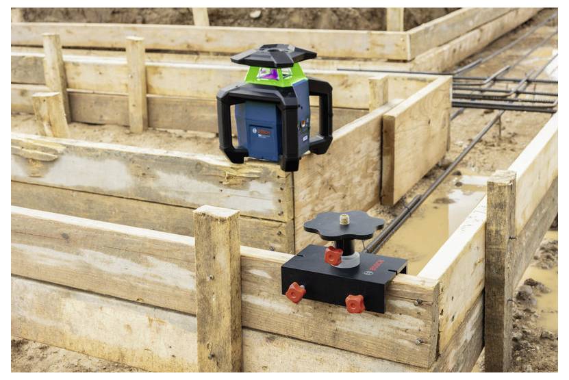 Laser level and receiver mounted on wooden formwork at a construction site, used to align foundations or walls.