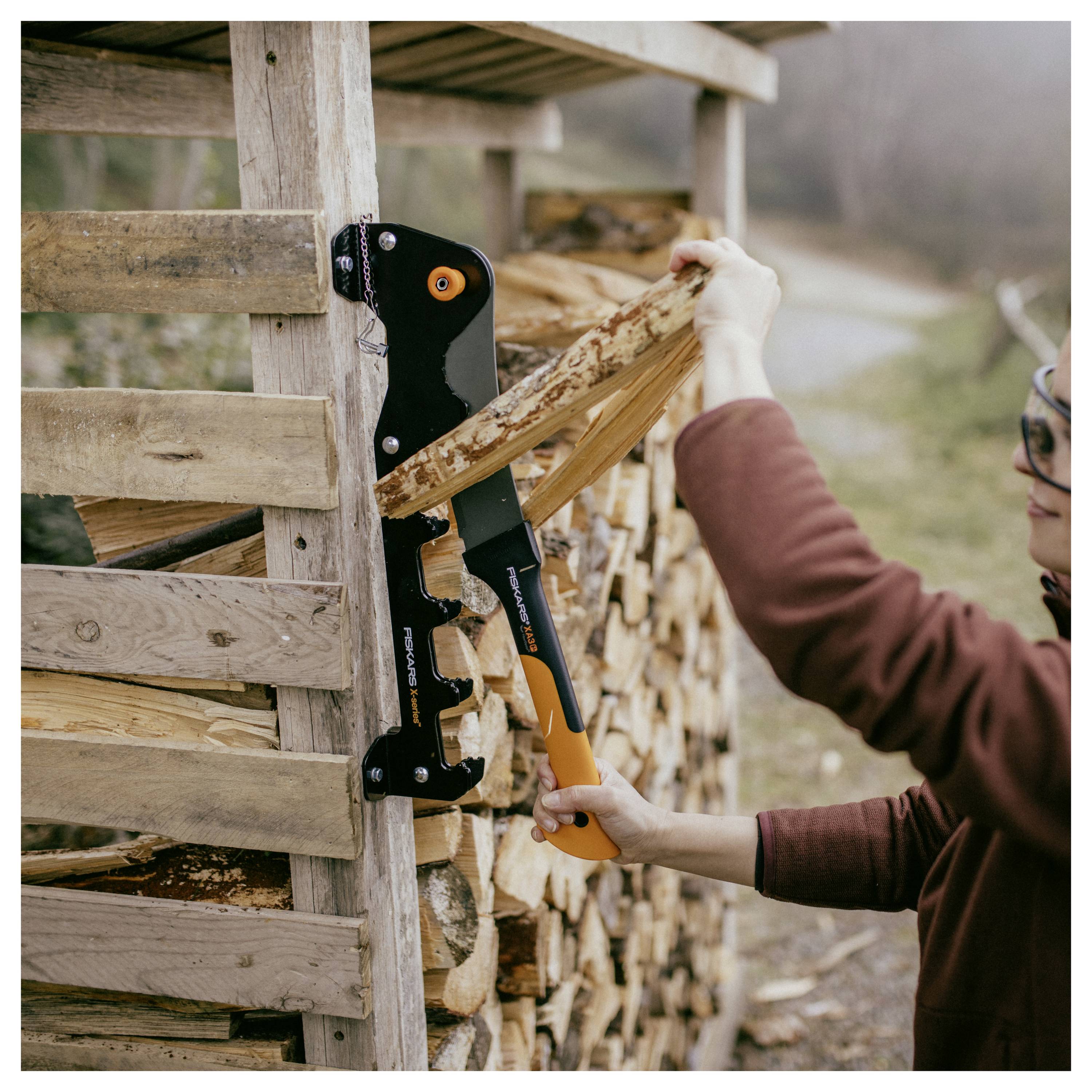 Une personne utilisant un séparateur de bois manuel pour fendre du bois de chauffage empilé à côté d'un hangar en bois à l'extérieur.
