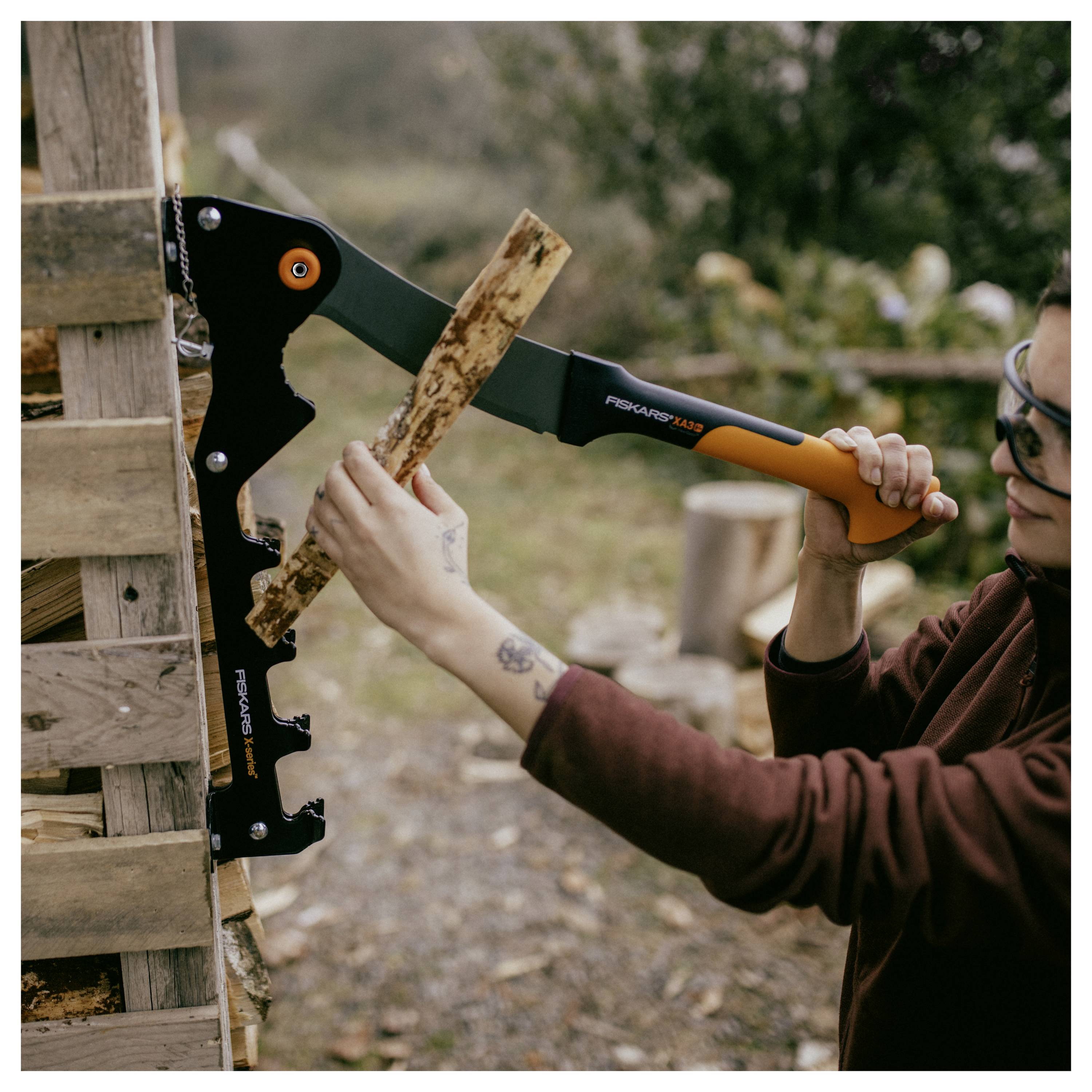 Personne utilisant une hache Fiskars x27 pour fendre du bois sur un billot de sciage en plein air.