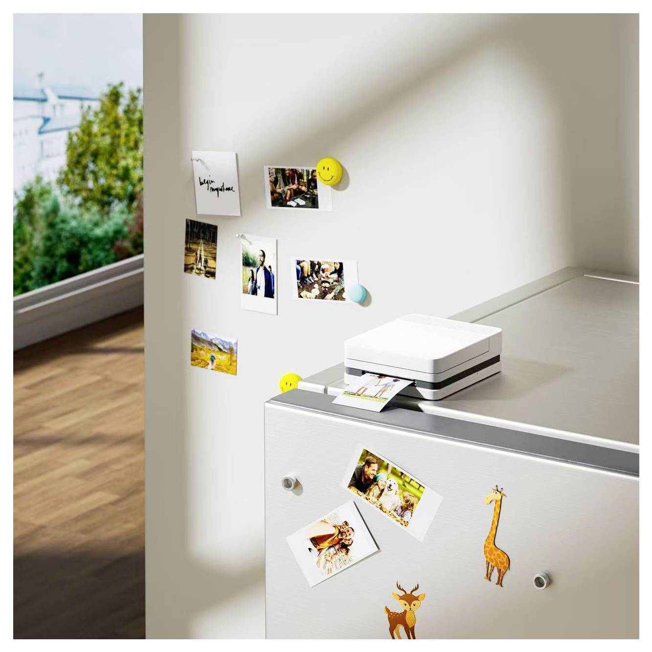 Petit imprimante photo blanc sur un meuble avec de petites photos imprimées et des aimants en forme d'animaux, à côté d'un mur affichant des clichés épinglés près d'une fenêtre baignée de soleil.