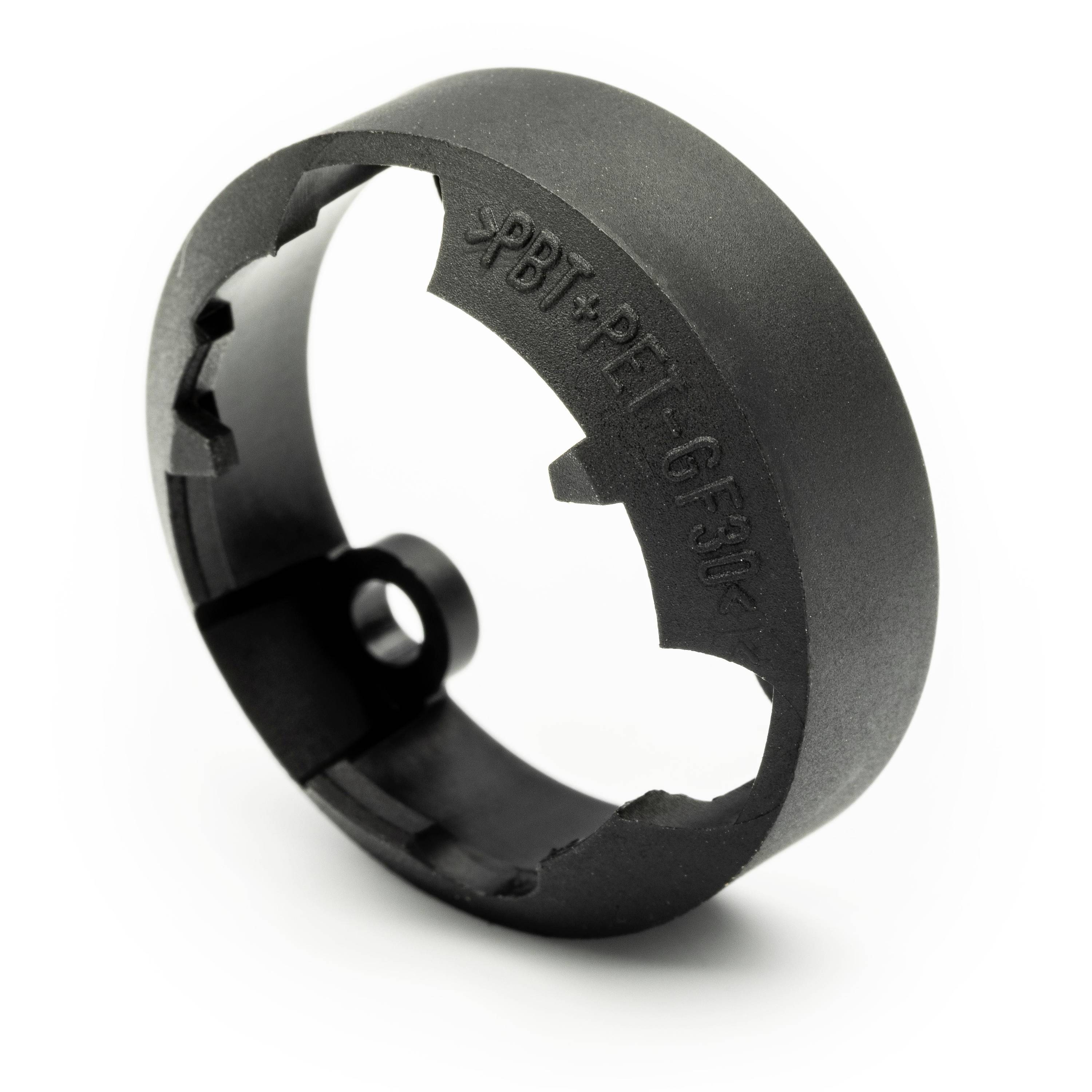 Black plastic ring-shaped mechanical part with a notched inner edge and embossed text on a white background.