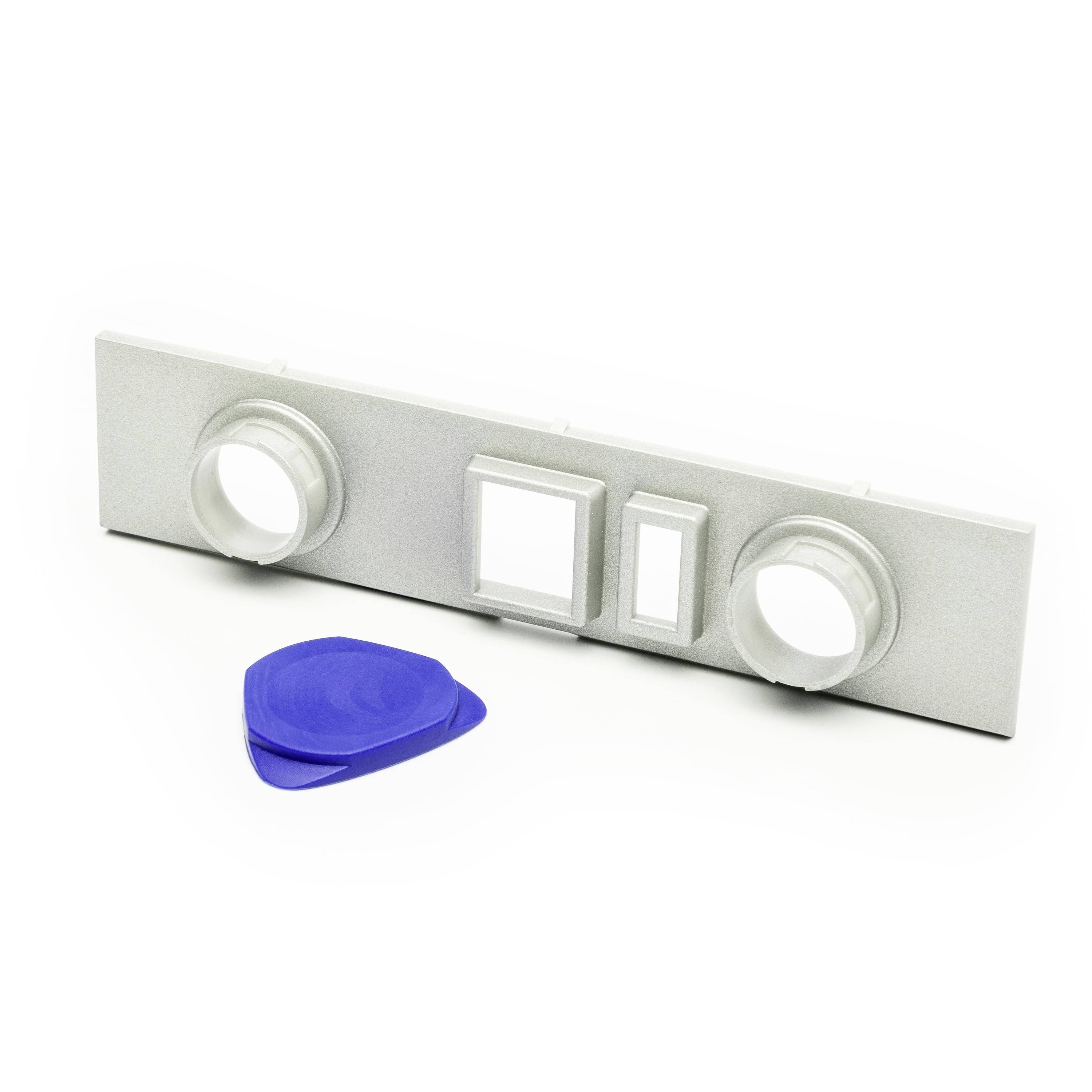 Silver rectangular panel with two round openings and two square inserts, shown with a blue plastic pry tool on a white background.