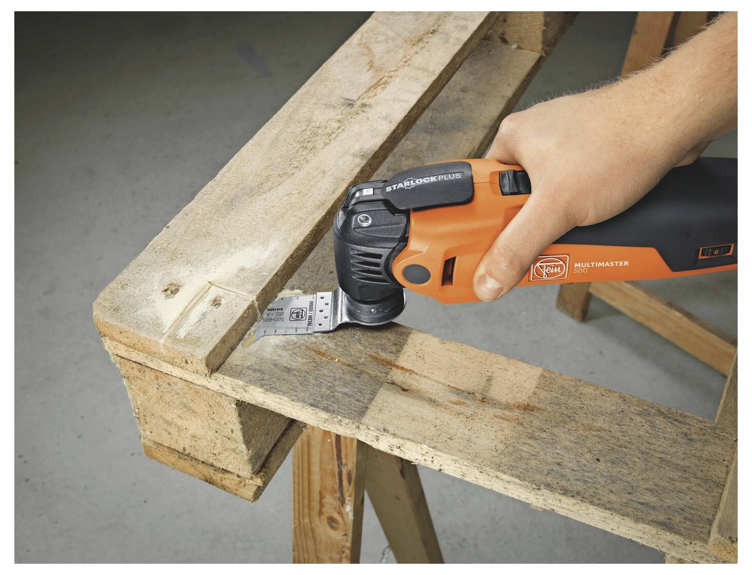 Une personne utilise un outil multifonction orange oscillant pour découper une entaille dans une poutre ou une planche en bois lors de travaux de menuiserie.