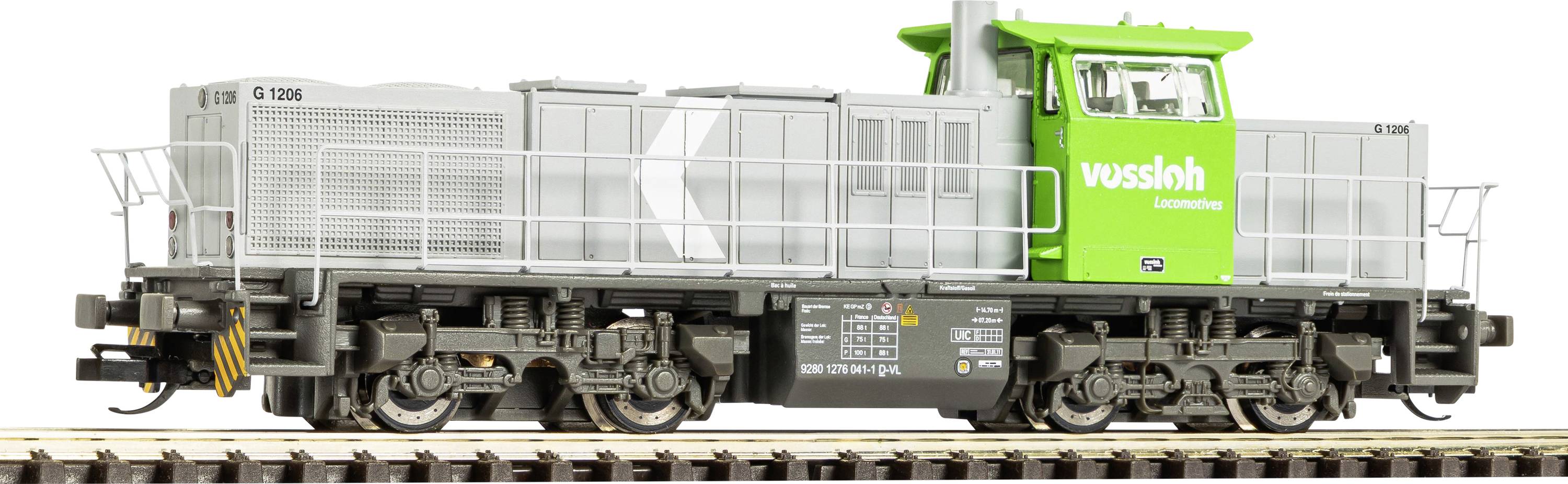 Vue latérale d'une locomotive Vossloh verte et grise sur fond blanc, montrant le moteur et l'ensemble des roues.