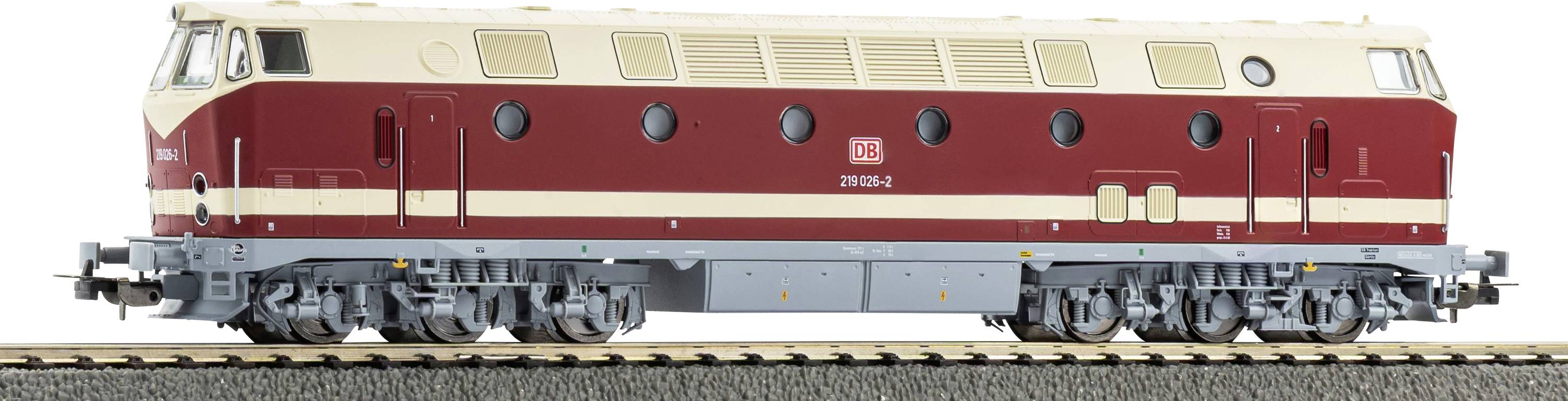Vue de côté d'une locomotive diesel rouge et crème sur des rails, présentée sur un fond blanc uni.
