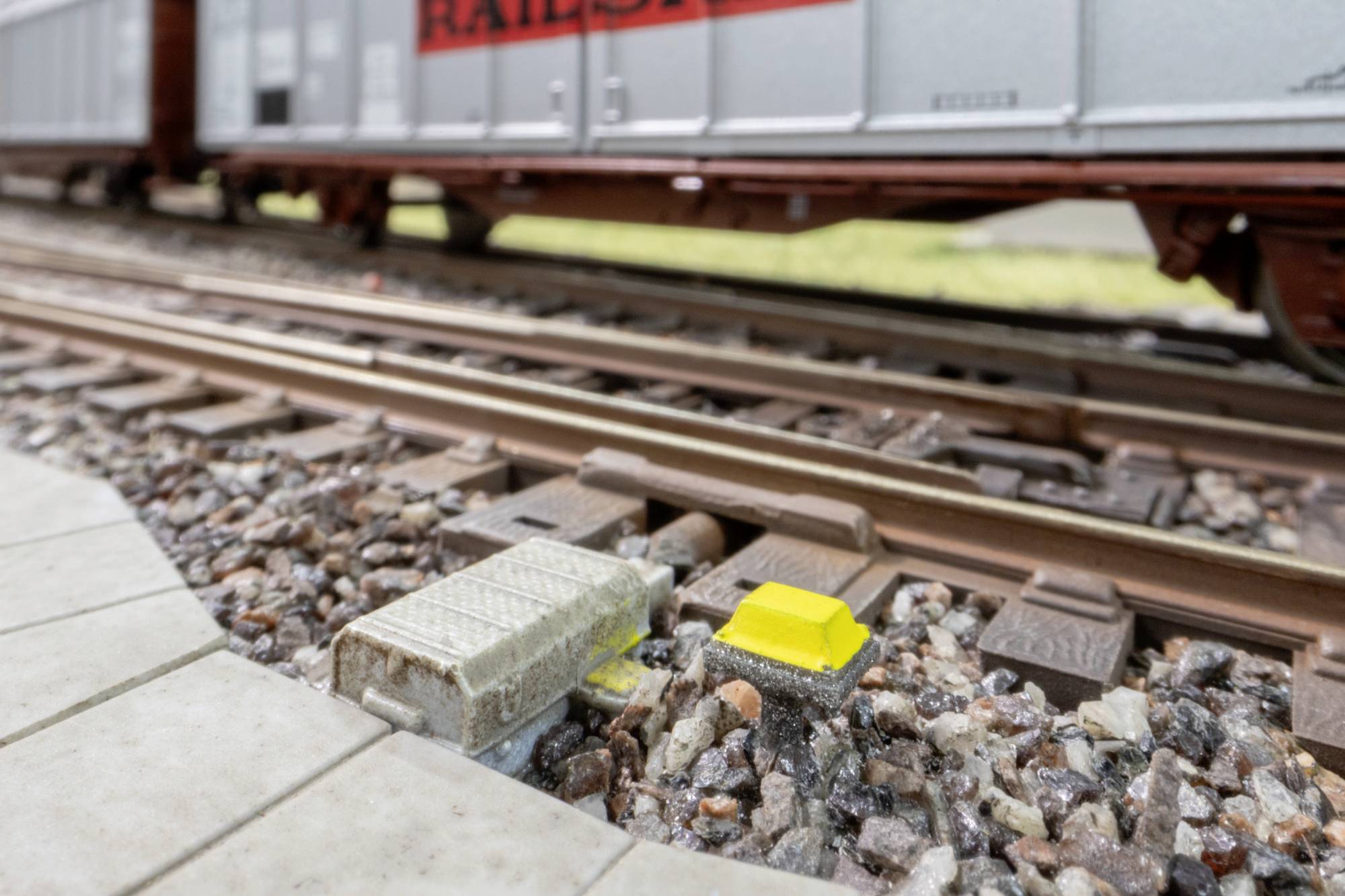 Gros plan de l'équipement de signalisation des voies ferrées à côté des rails de chemin de fer, avec un wagon de marchandises flou passant en arrière-plan.