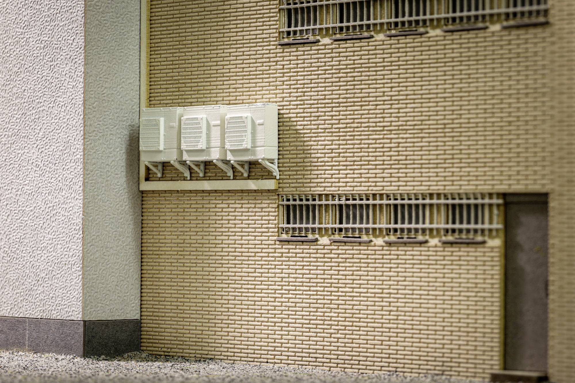 Façade de petit bâtiment avec trois unités de climatisation murales et fenêtres à barreaux sur un mur de briques.