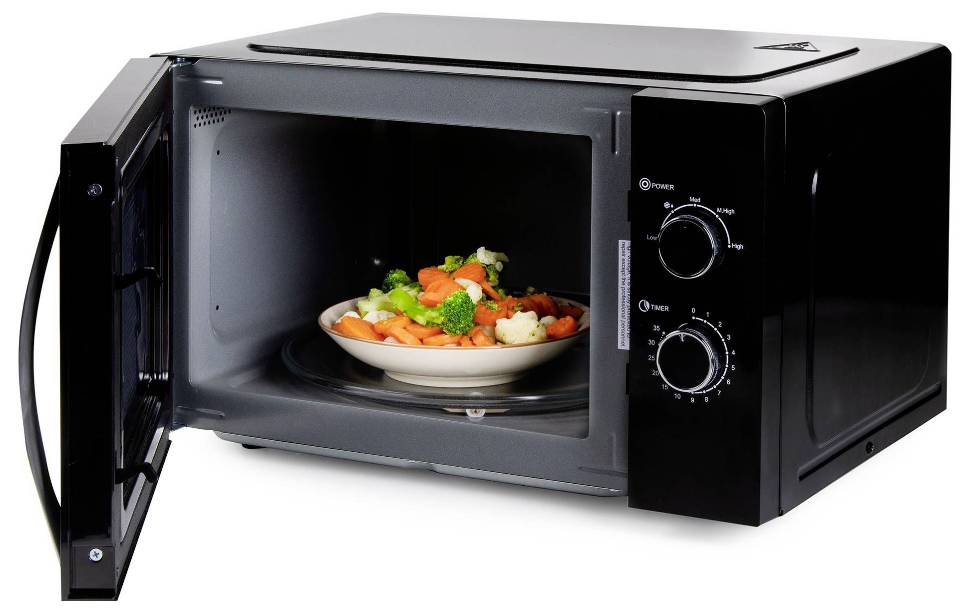 Open black microwave oven with a plate of mixed vegetables inside on the glass turntable, door swung open to the left.