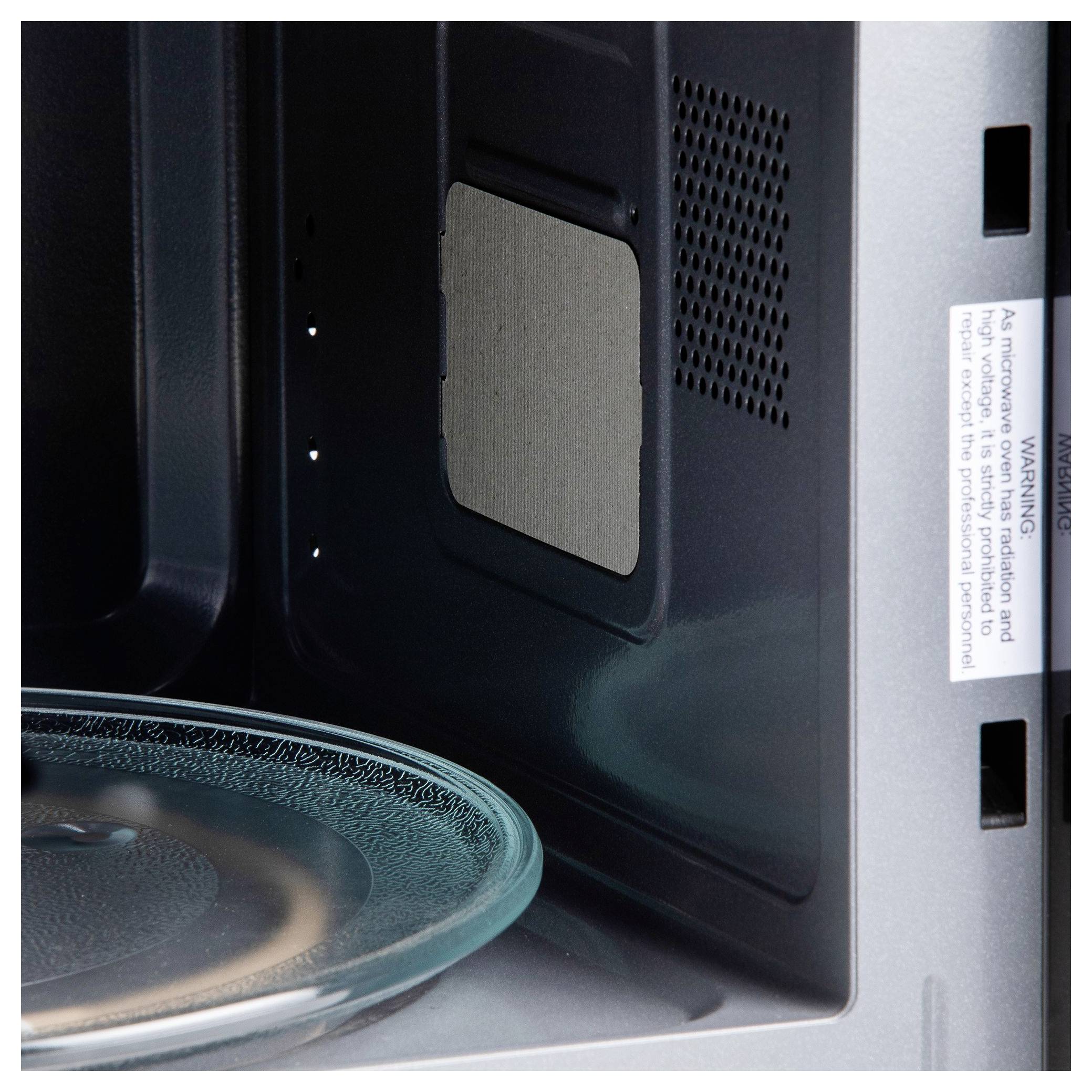 Inside a microwave oven, a glass plate is visible on the turntable with the interior wall and warning label shown.