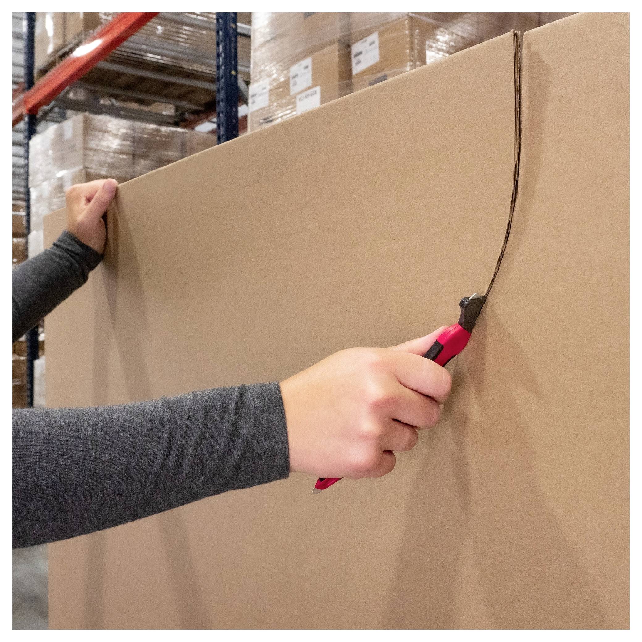 Person uses a red utility knife to cut open a large cardboard box in a warehouse.
