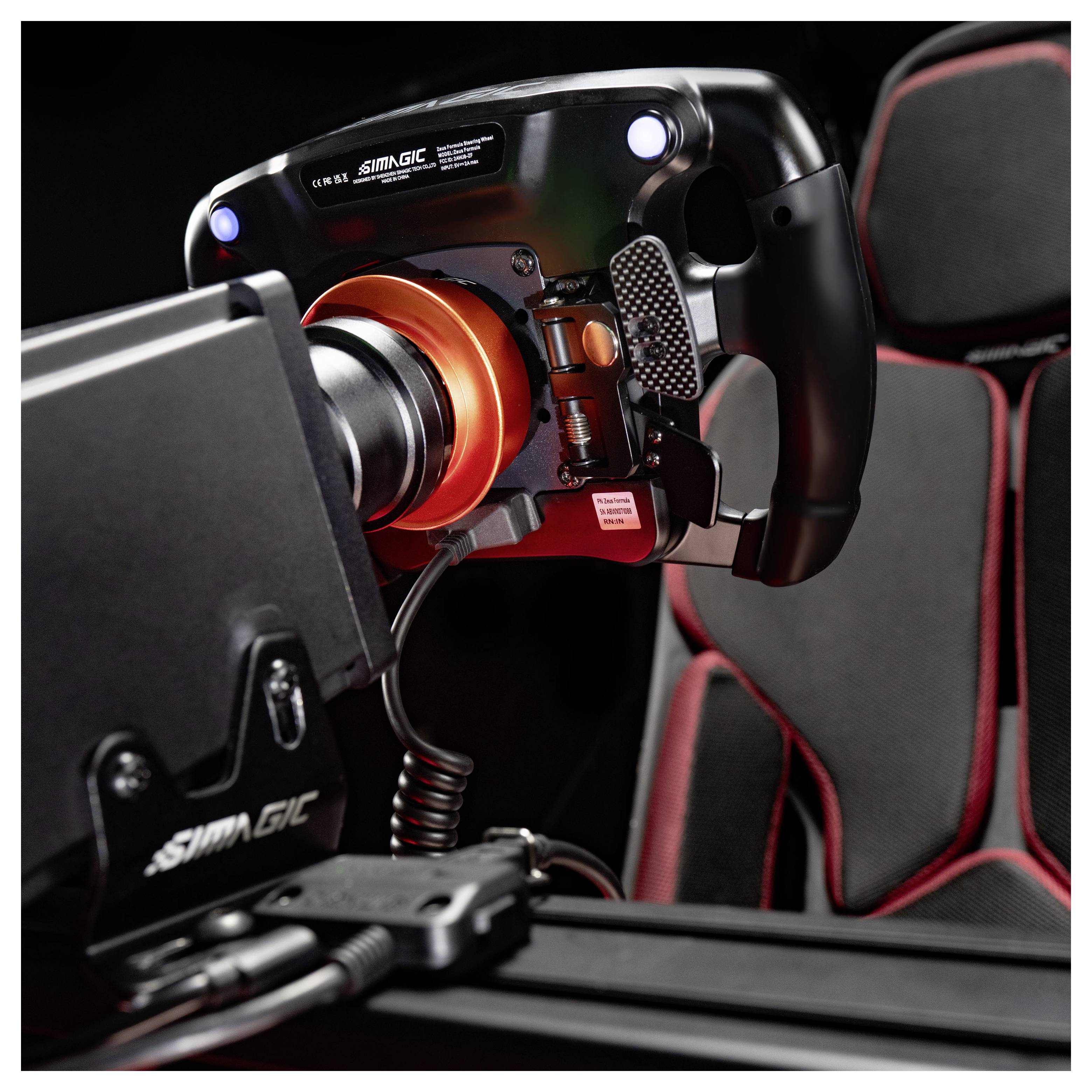 Gros plan d'un volant de simulation de course SIMAGIC monté sur une installation de conduite, avec un siège baquet noir et rouge en arrière-plan.