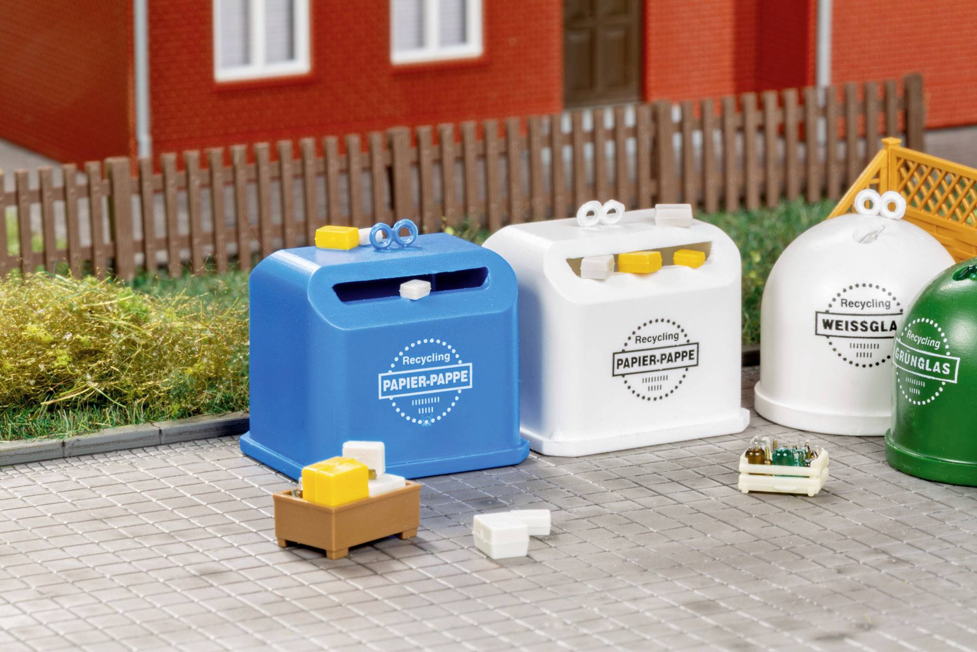 Petits bacs de recyclage pour le papier, le verre et les déchets mixtes alignés à l'extérieur à côté d'une clôture et d'un mur de maison.