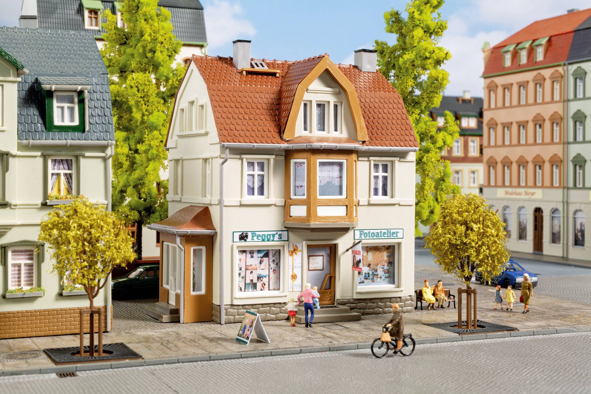 Petite scène de rue avec une épicerie de coin nommée « Peggy's Potzbackerei », de petites figurines marchant et faisant du vélo sur une rue de maquette de ville.