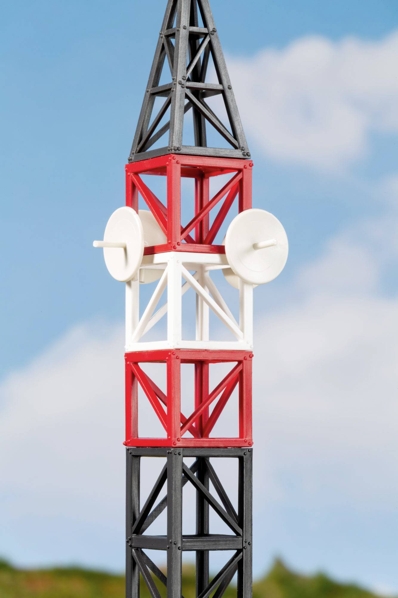 Gros plan d'une tour de télécommunications rouge, blanche et noire avec deux antennes paraboliques blanches contre un ciel bleu.