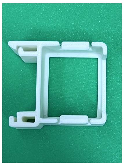 Cadre de montage en plastique blanc ou clip sur un fond texturé vert, montré en gros plan.