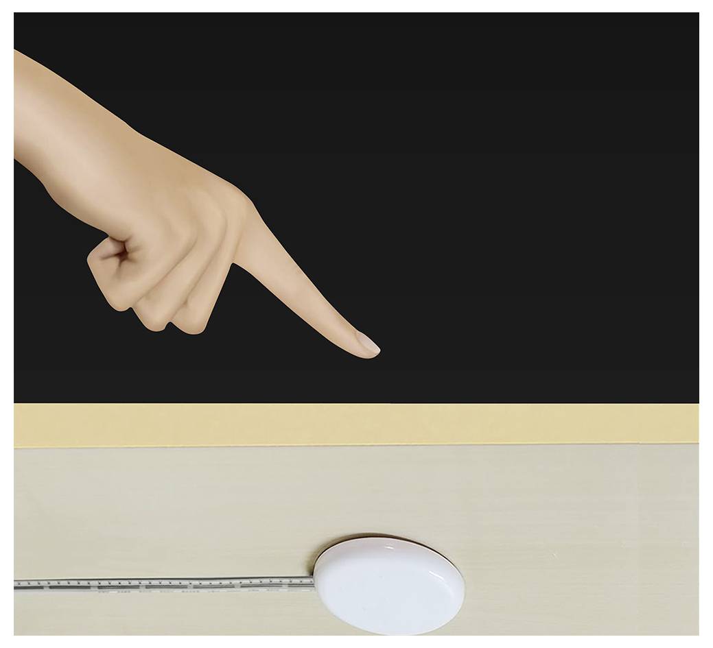 Une main pointe vers un objet ovale blanc sur une surface claire, avec une règle le long du bord inférieur contre un fond sombre.