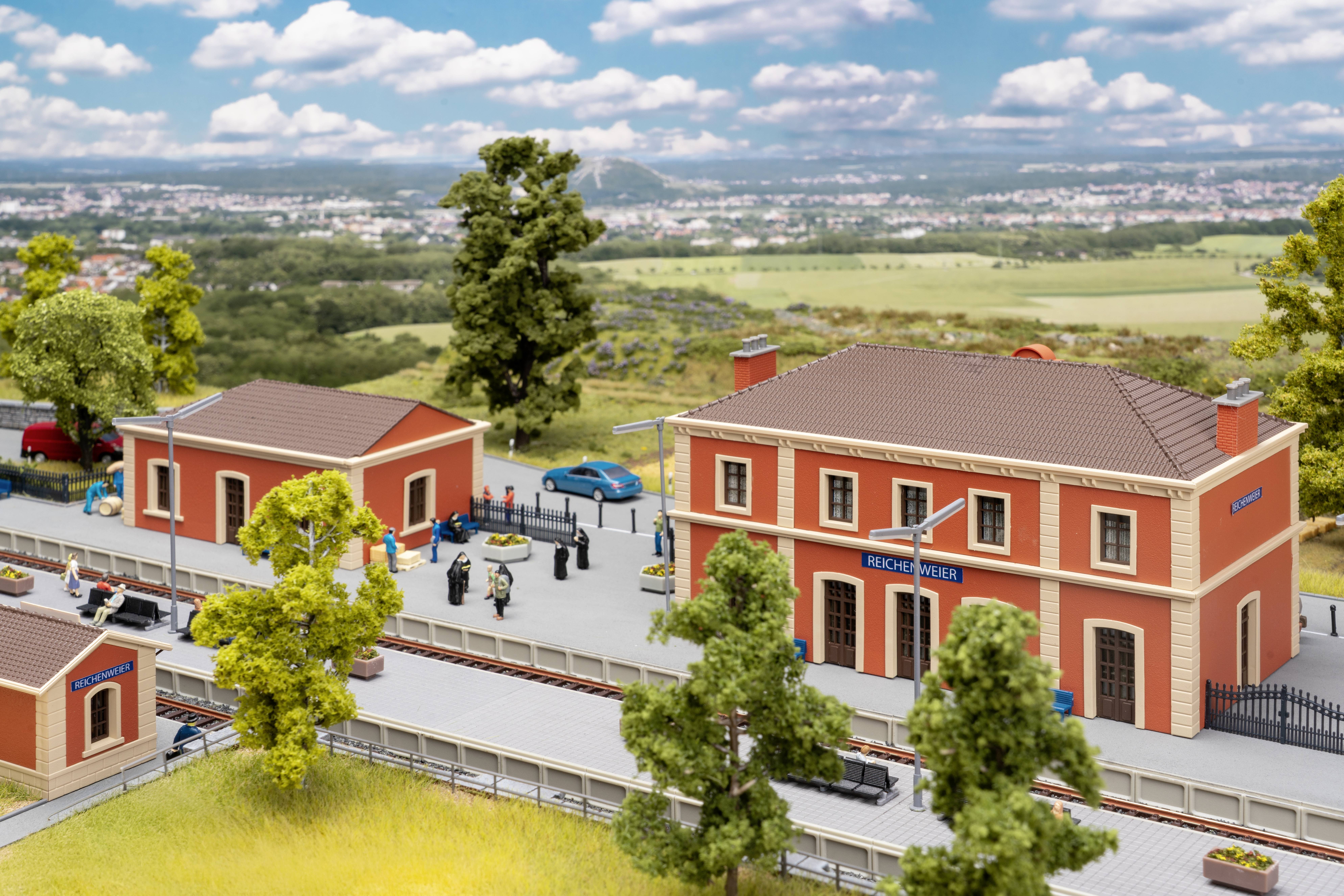 Modèle miniature d'une gare ferroviaire de Beechy View avec des bâtiments orange, un quai, des personnes, des voitures et des voies ferrées dans un paysage rural.