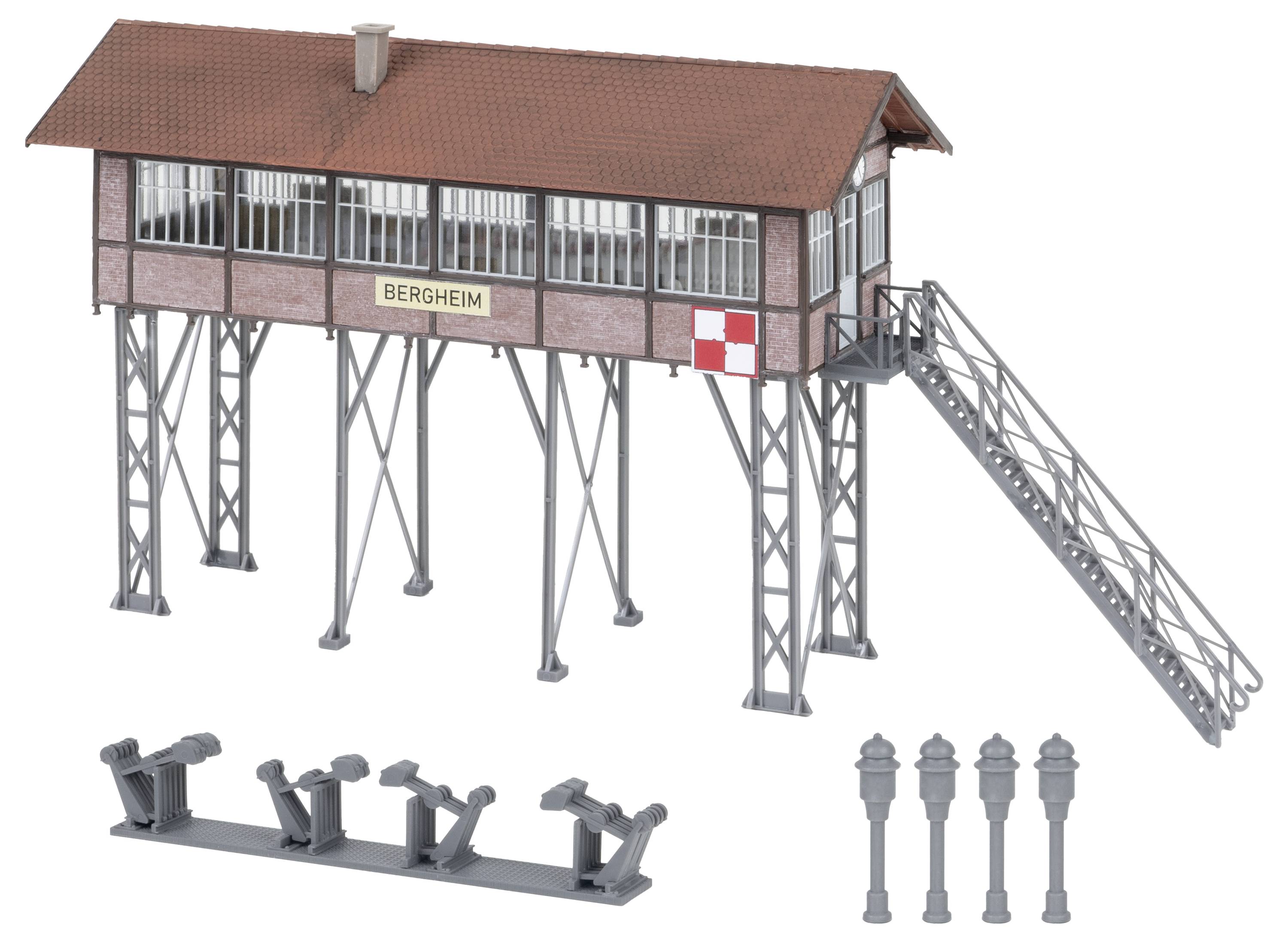 Maquette d'une cabine de signalisation ferroviaire surélevée portant l'étiquette « BERGHEIM » avec escaliers, ainsi que des appareils de commutation de voie séparés et des lampadaires affichés ci-dessous.