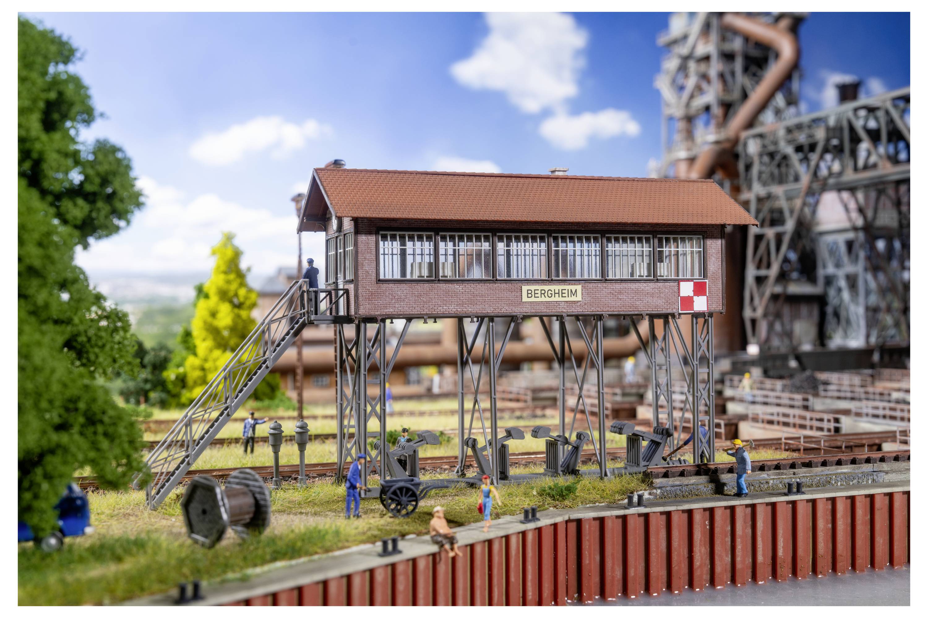 Scène industrielle miniature avec un bâtiment surélevé étiqueté « BERGHEM », des ouvriers, des voies et des machines dans un décor de chemin de fer miniature.