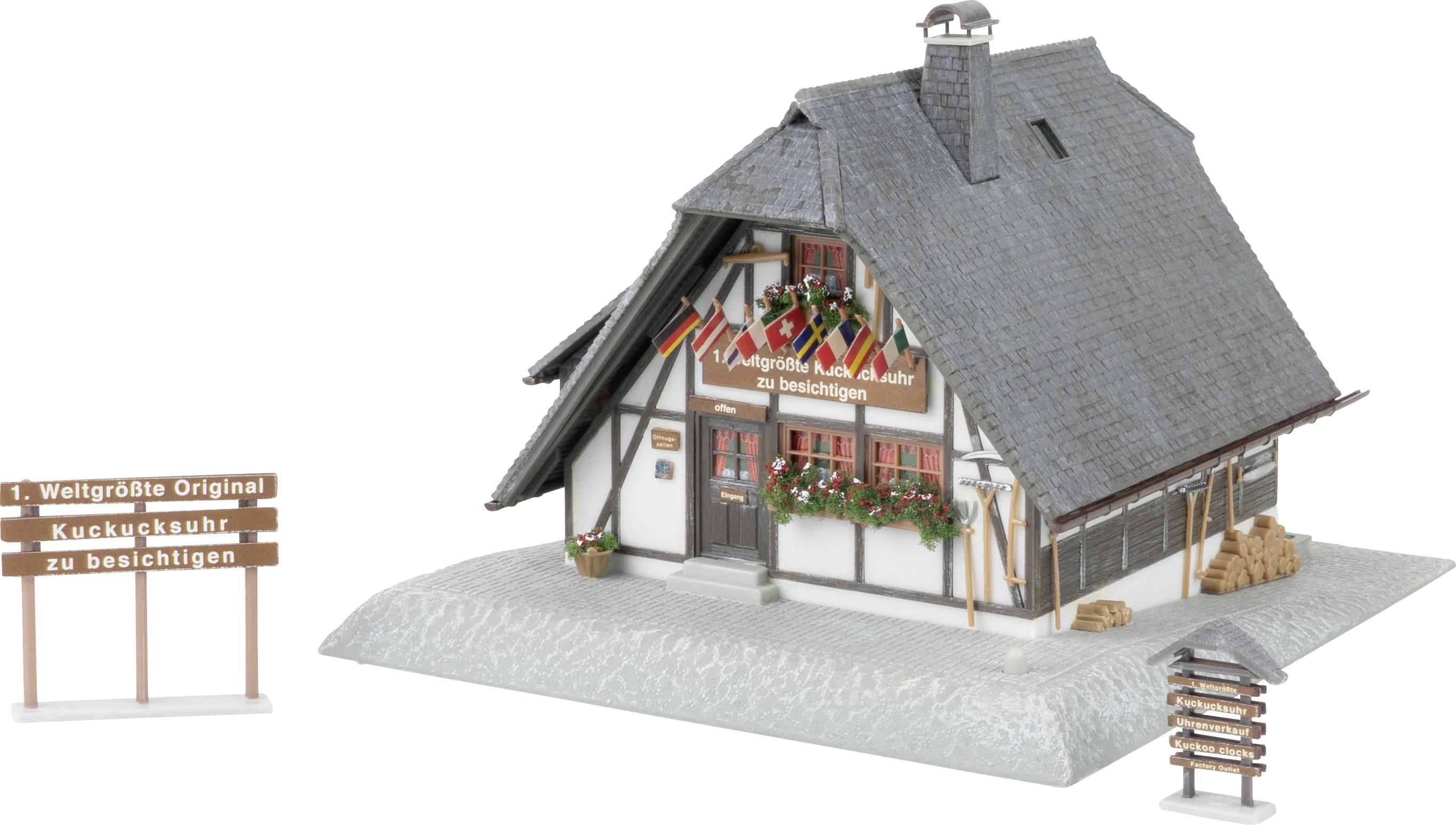 Maquette d'une petite maison à colombages avec un toit en pente raide, des jardinières fleuries, et des pancartes lisant « 1. Plus grande coucou du monde original à voir » et « 2. à voir également ici ».