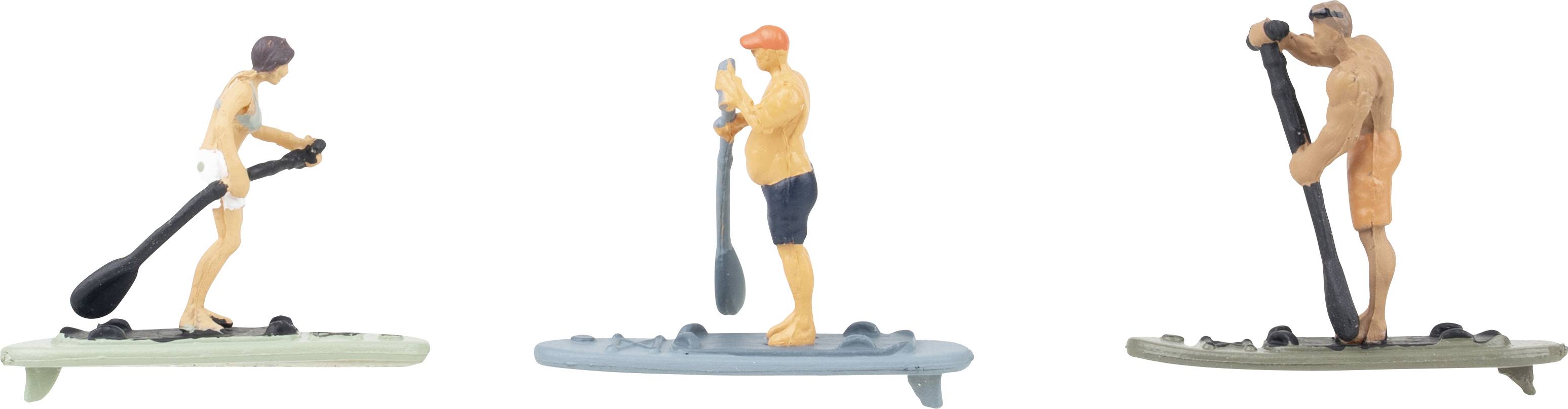 Trois figurines d'une personne utilisant une planche de paddle debout : une sur une planche verte, une sur une planche bleue et une sur une planche grise.