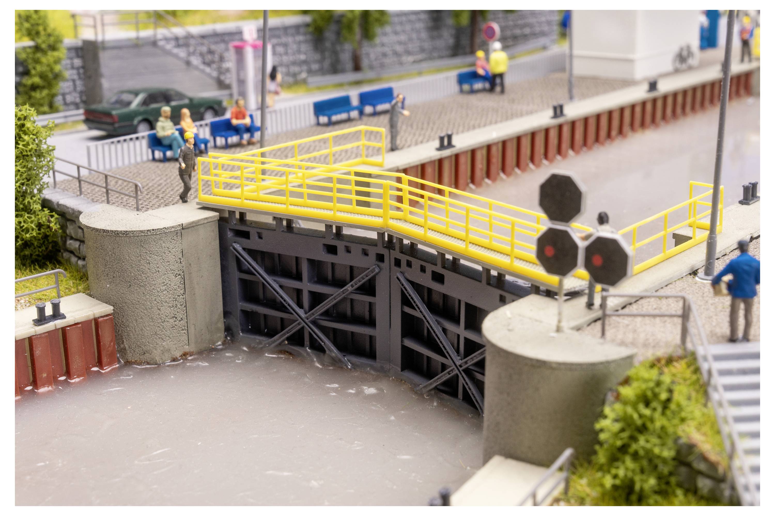 Écluse de modèle réduit dans une scène de canal miniature, avec des rampes jaunes, de l'eau en dessous, et de minuscules personnes debout à proximité.