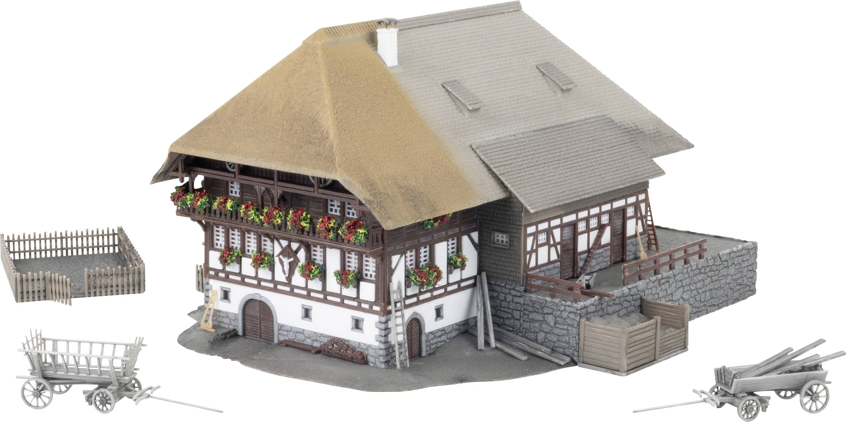 Maquette d'une ferme traditionnelle avec un toit de chaume, des jardinières de fleurs, une cour clôturée, et de petits chariots agricoles à côté sur un fond blanc.