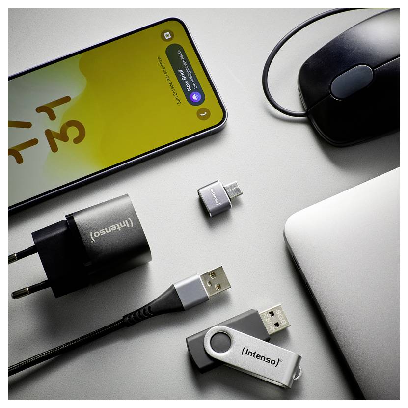 Un smartphone connecté à plusieurs adaptateurs USB et câbles à côté d'une souris et d'un ordinateur portable, illustrant la charge des appareils et la connectivité.