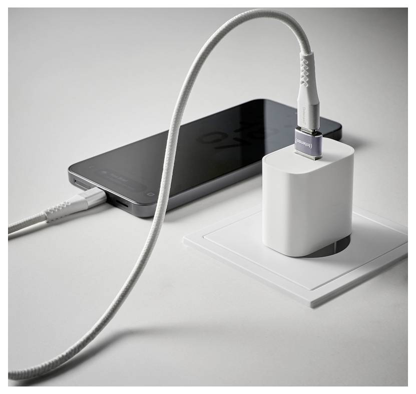 Un téléphone intelligent se charge à côté d'un adaptateur mural blanc sur un bureau, avec deux câbles connectés au téléphone et au chargeur.