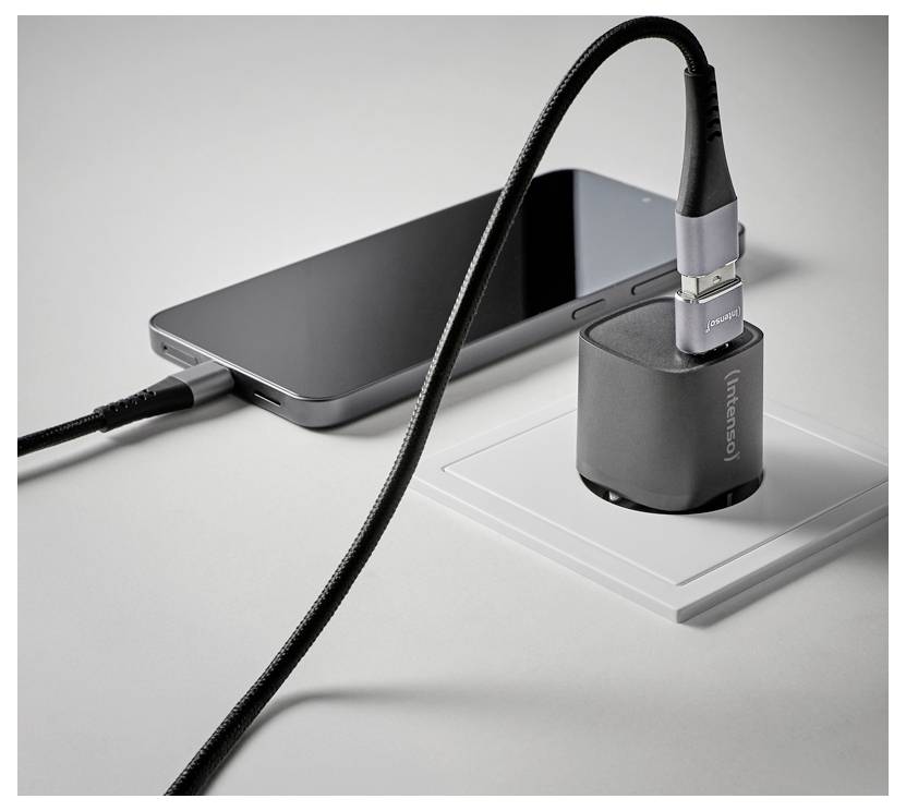Chargement d'un smartphone sur un bureau via un câble USB noir connecté à un socle de recharge sans fil gris.