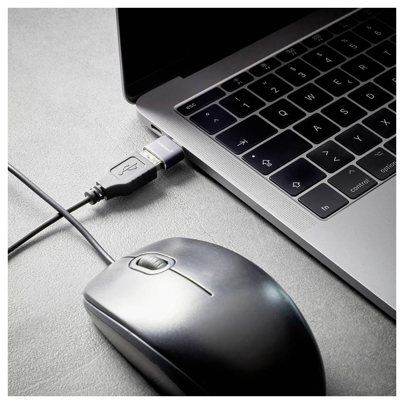 Gros plan d'un ordinateur portable avec un câble USB branché et une souris d'ordinateur à côté sur un bureau gris.