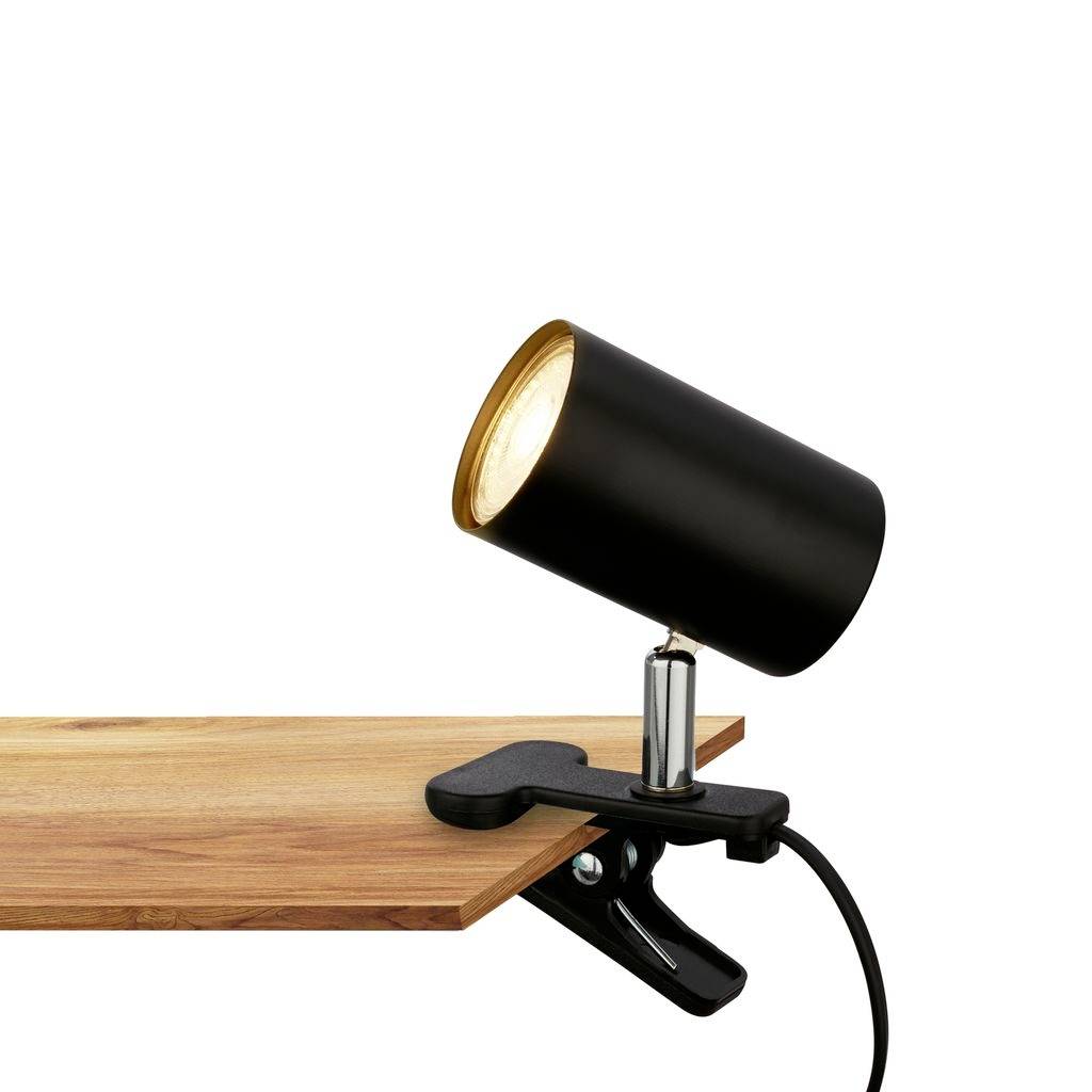 Lampe projecteur à pince noire fixée à une surface en bois, orientée vers le haut et allumée.