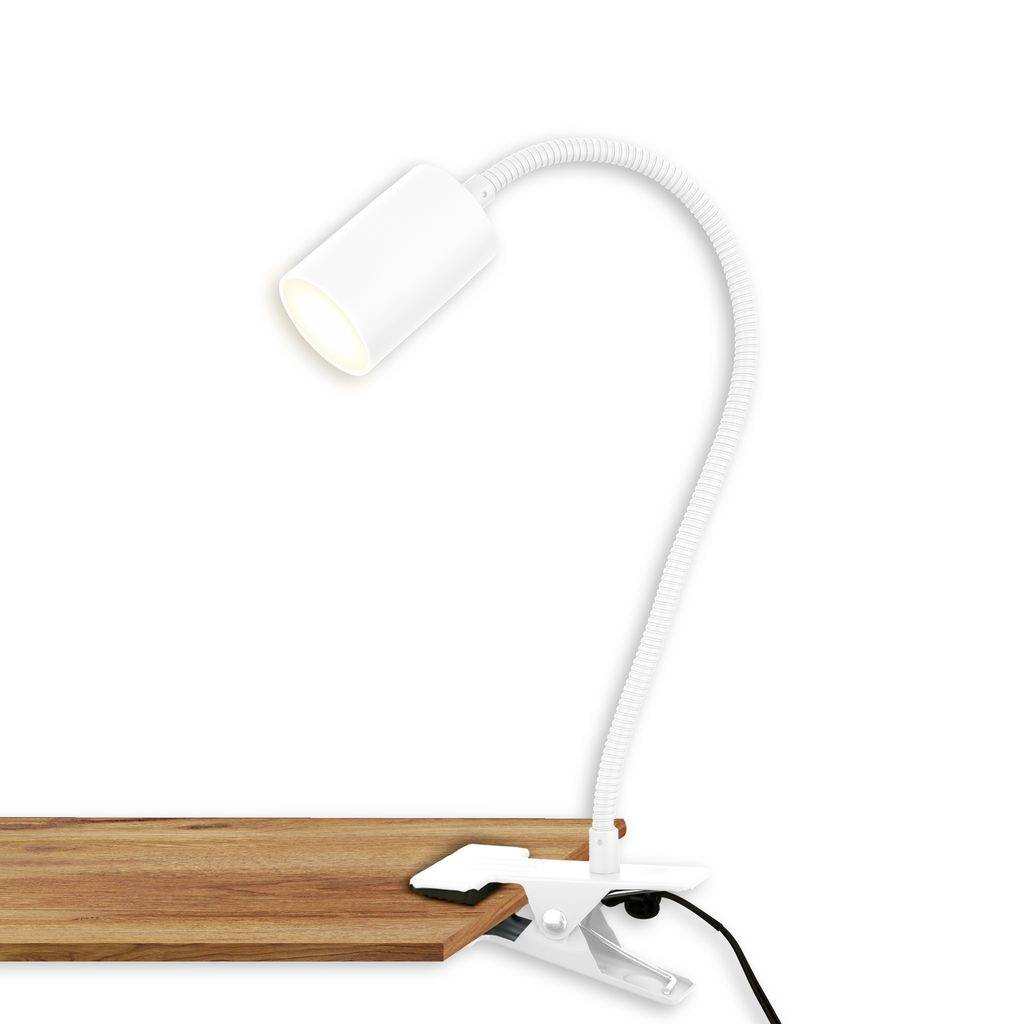 Lampe clip blanche avec un col flexible fixée au bord d'un bureau en bois, avec sa lumière allumée.