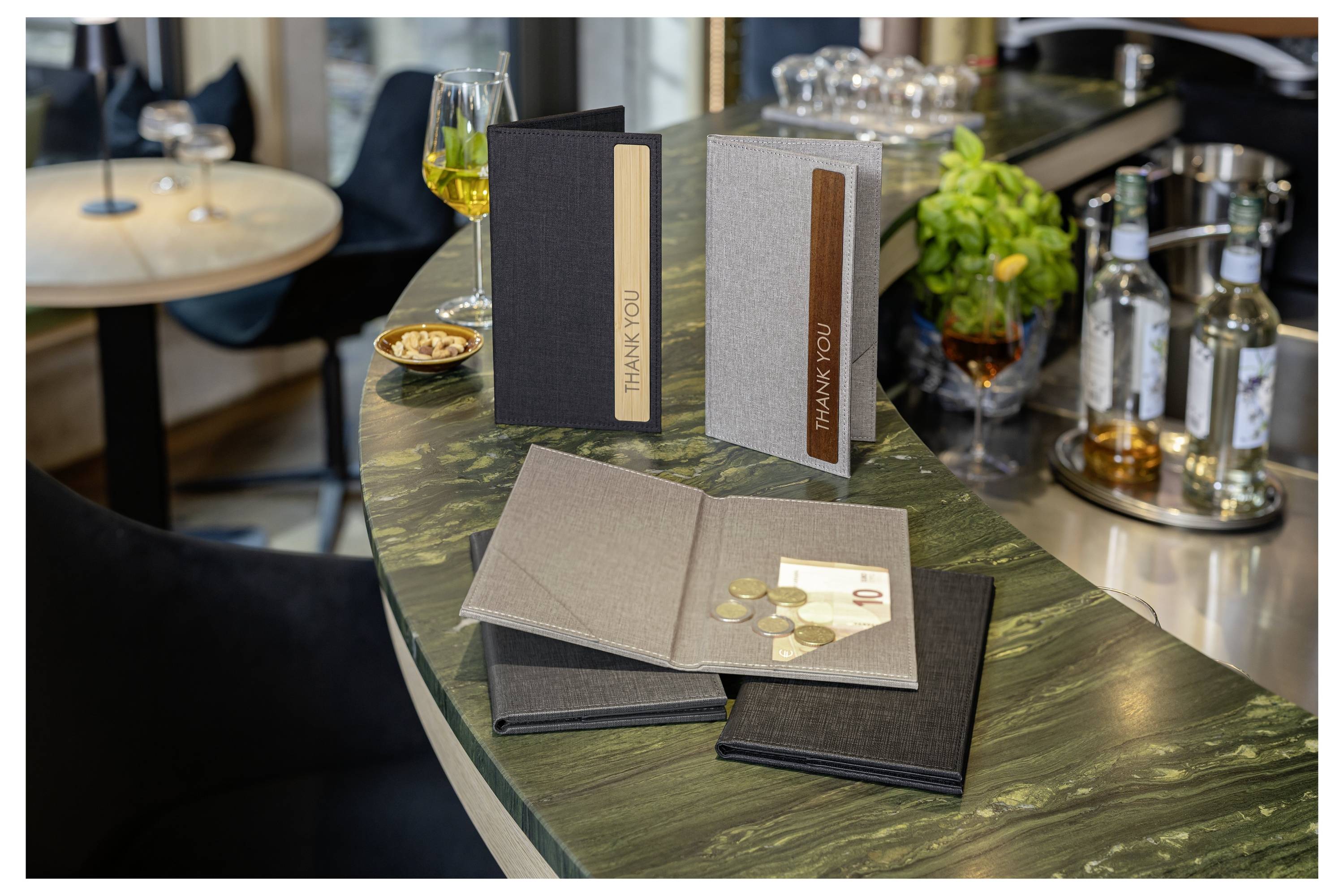 Table setting with four thank-you cards, one open with coins and cash inside, on a restaurant counter near drinks and condiments.