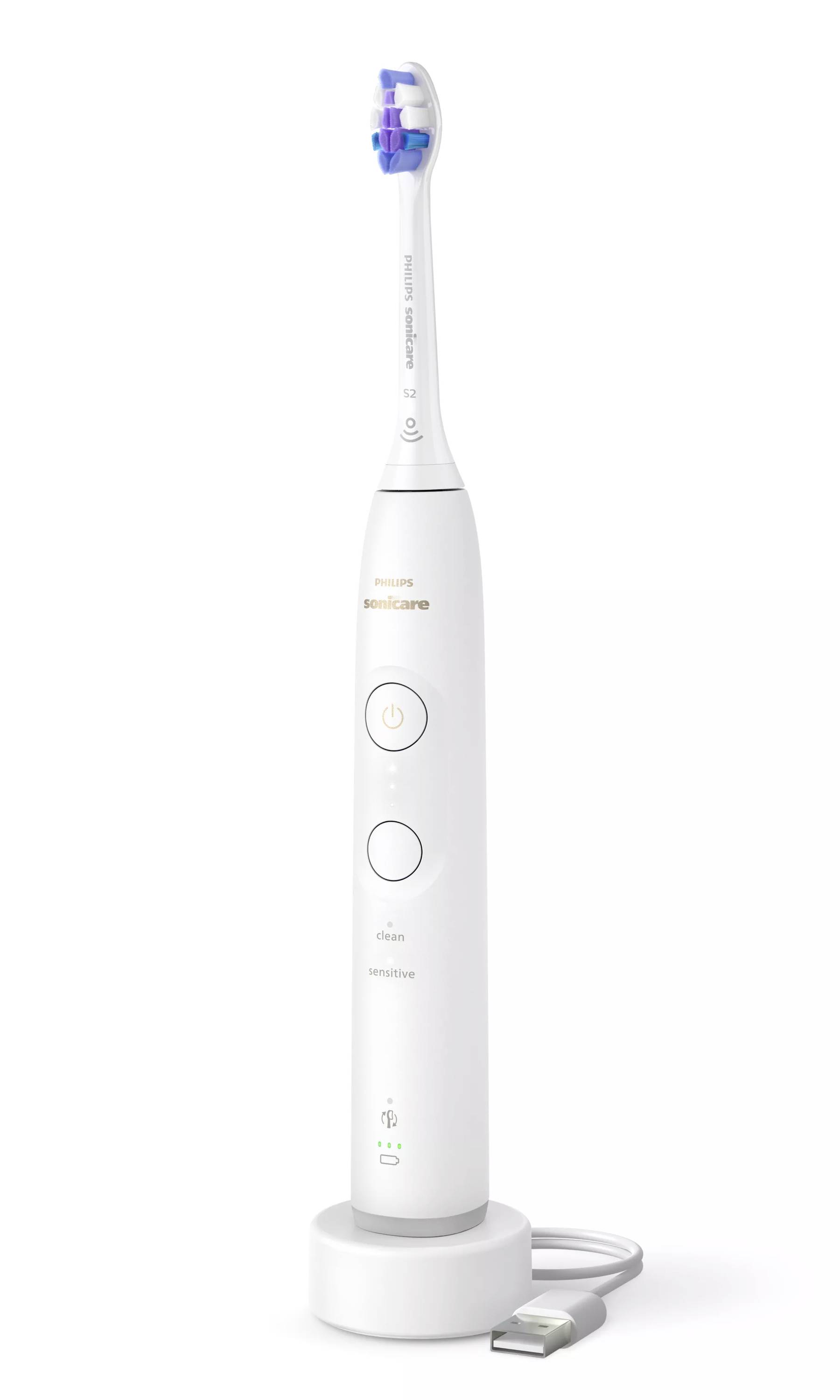 Brosse à dents électrique blanche posée sur un socle de charge avec un câble USB attaché.