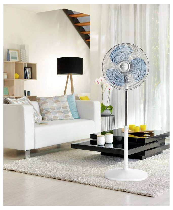 Ventilateur de socle blanc dans un salon moderne et lumineux à côté d'un canapé, d'un lampadaire, d'une table basse et de rideaux en mousseline.