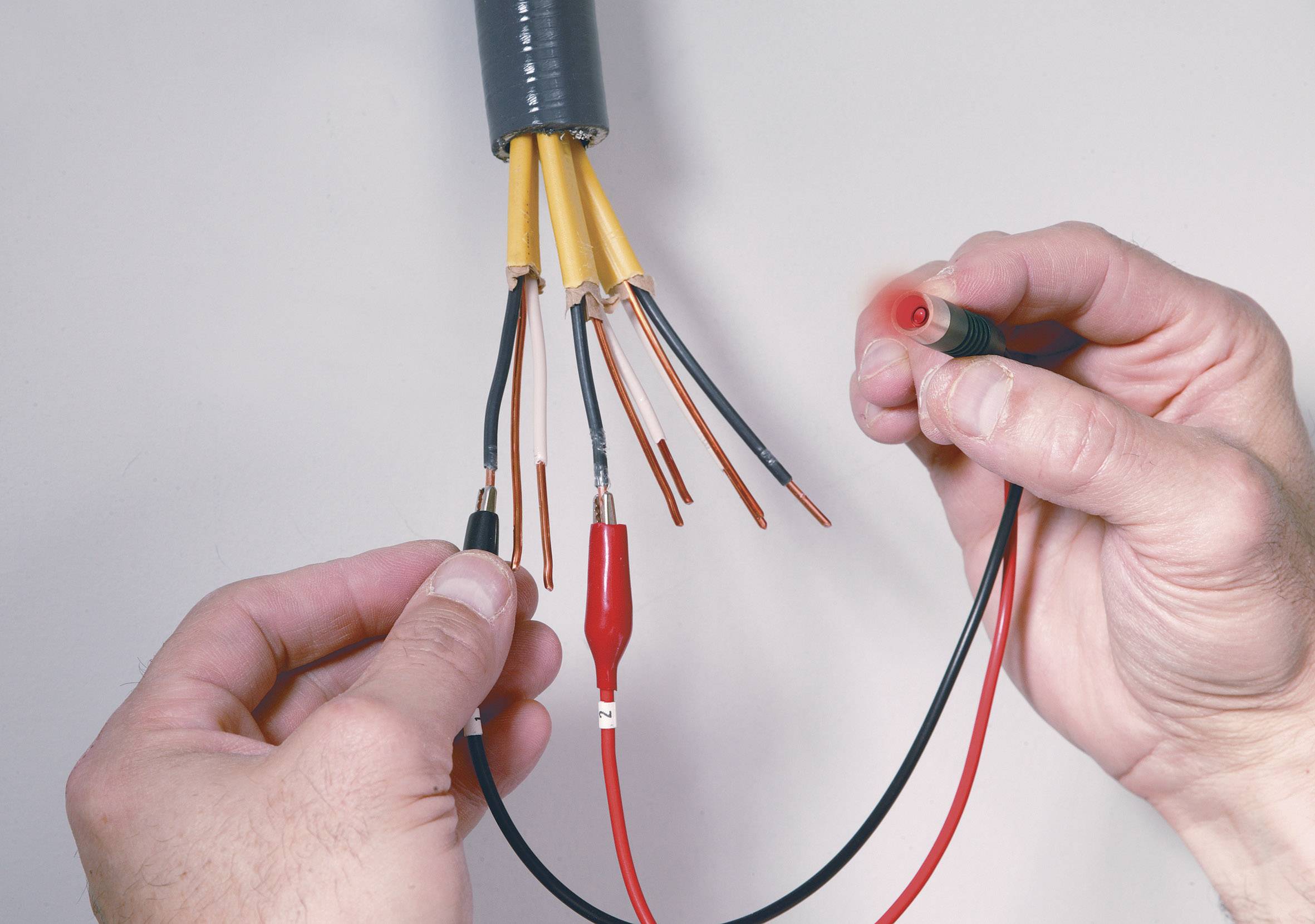 Une personne mesure la tension de plusieurs câbles dénudés à l'aide d'un multimètre afin de vérifier leur connexion électrique.
