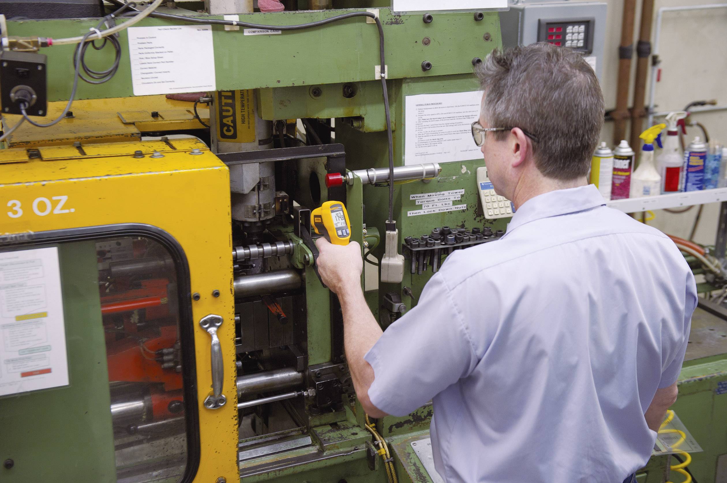 Un homme utilise une grande machine industrielle dans une usine. Il se sert d'un instrument de mesure pour effectuer un contrôle.