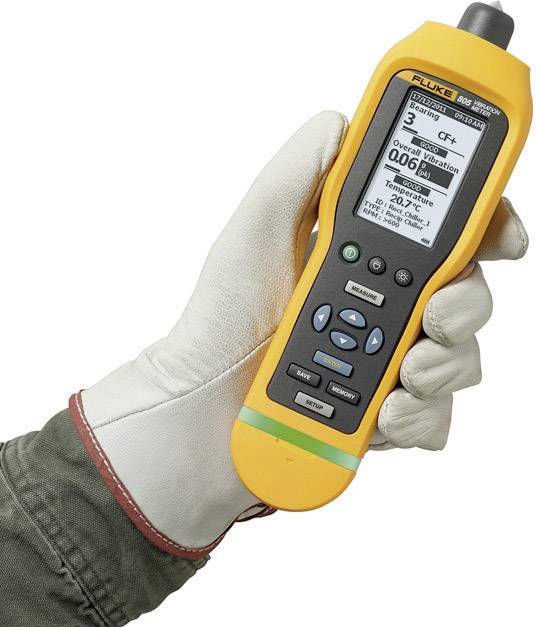 Une main gantée tient un appareil de mesure jaune qui mesure les particules dans l'air. Il affiche une valeur de 0,06 Pm.