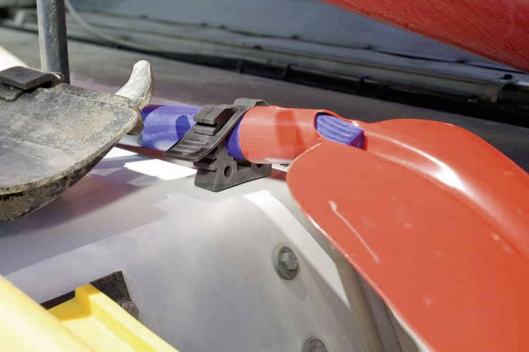 Pelles rouges et bleues, fixées à un porte-bagages de véhicule. Gros plan sur l'attache. L'environnement suggère des activités de plein air.