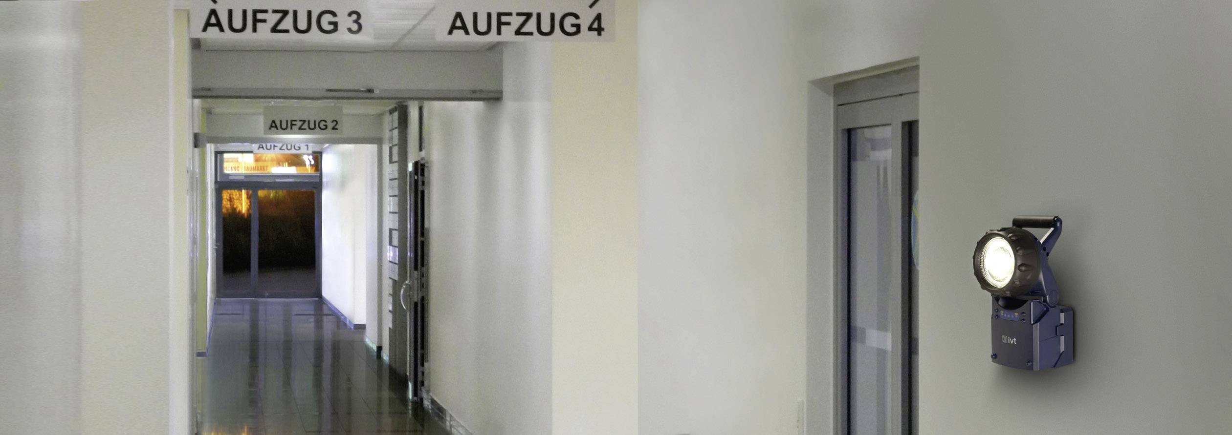 Un couloir avec des portes d'ascenseurs, étiquetées 'Ascenseur 2', 'Ascenseur 3' et 'Ascenseur 4'. Sur la gauche, on peut voir des portes vitrées menant à l'extérieur.