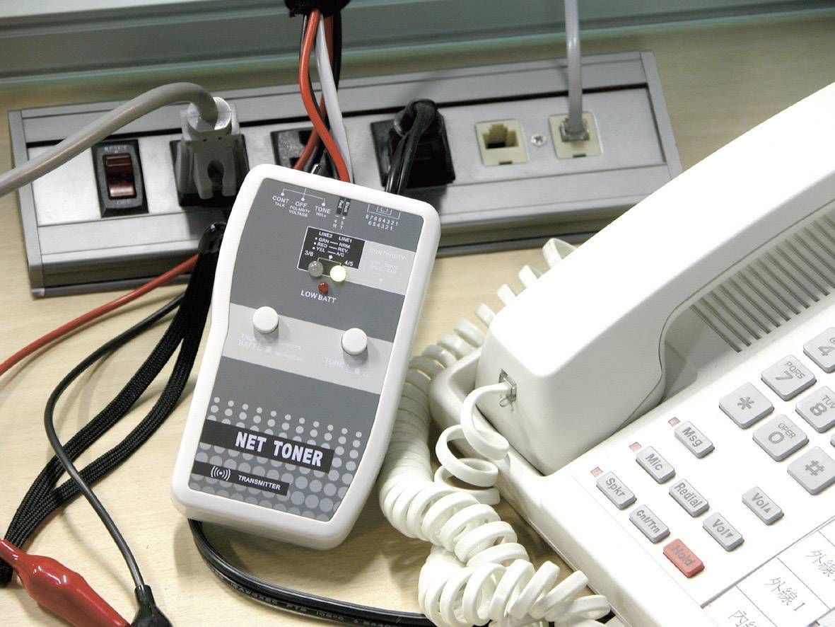 Un téléphone et des tonalités réseau sont posés sur un bureau, entourés de câbles et de prises électriques, illustrant un dispositif de maintenance technique ou d'installation.