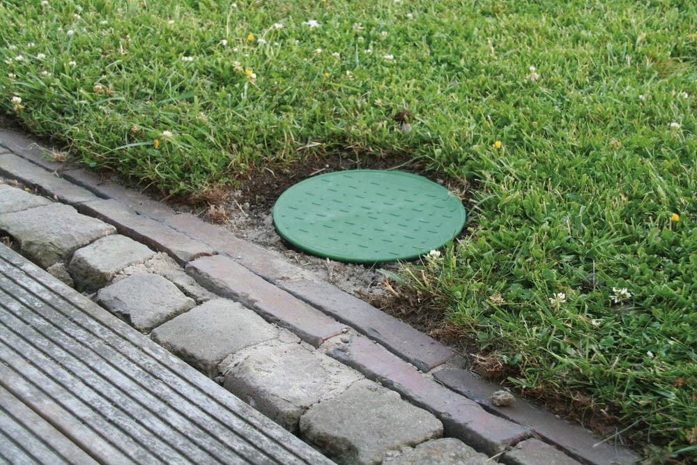 Un tampon d'égout vert dans l'herbe à côté d'un chemin pavé.