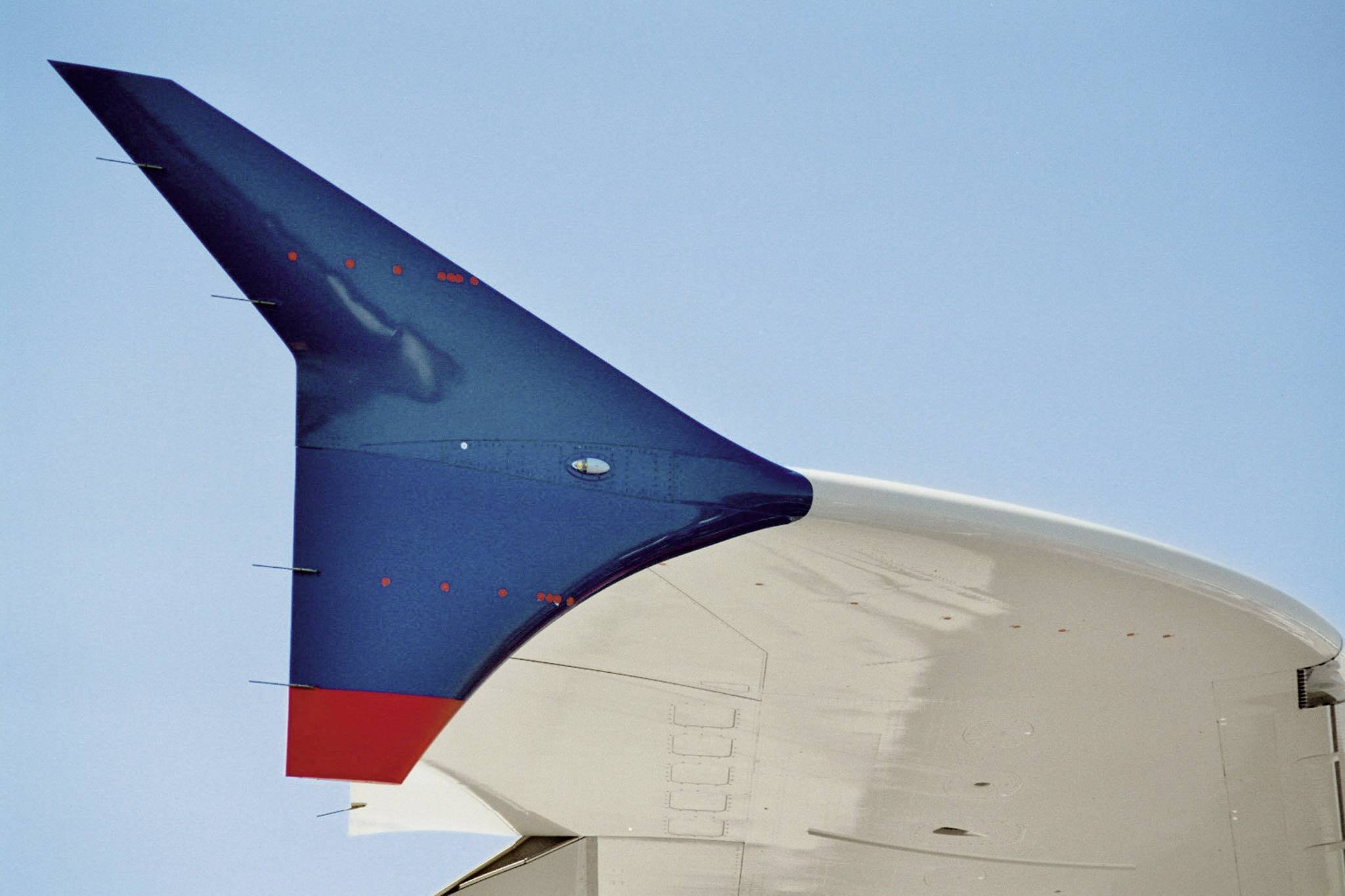 Un empennage bleu et rouge devant un ciel dégagé.