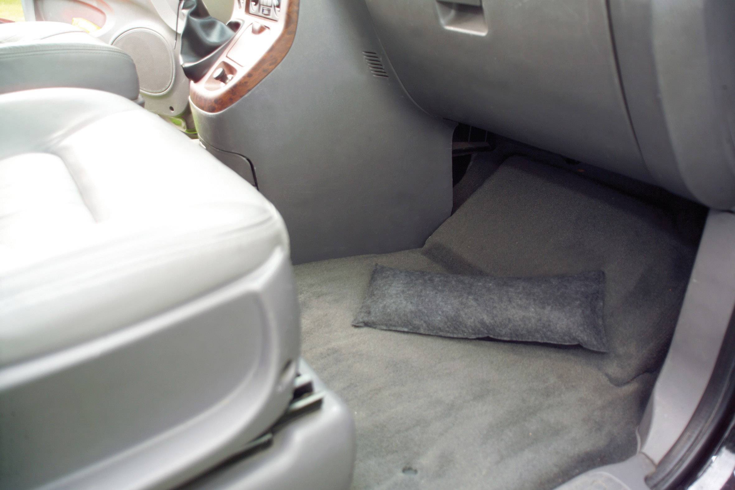 L'image montre l'espace au niveau des pieds du passager avant d'une voiture avec un petit coussin posé sur le sol. La zone est propre et bien rangée.