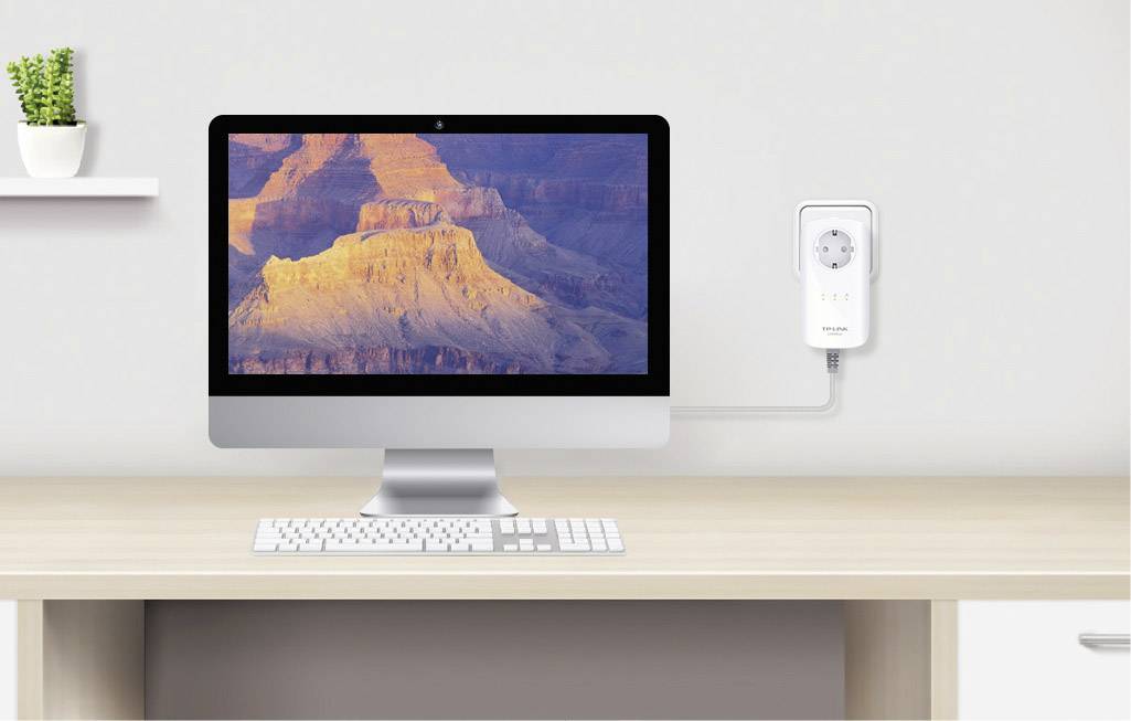 Un ordinateur sur une table avec un écran affichant le Grand Canyon. À côté, un adaptateur secteur blanc est branché au mur.