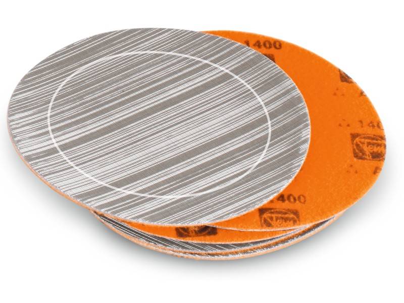 Une série de disques abrasifs gris et orange empilés les uns sur les autres. Le disque supérieur présente un motif linéaire.